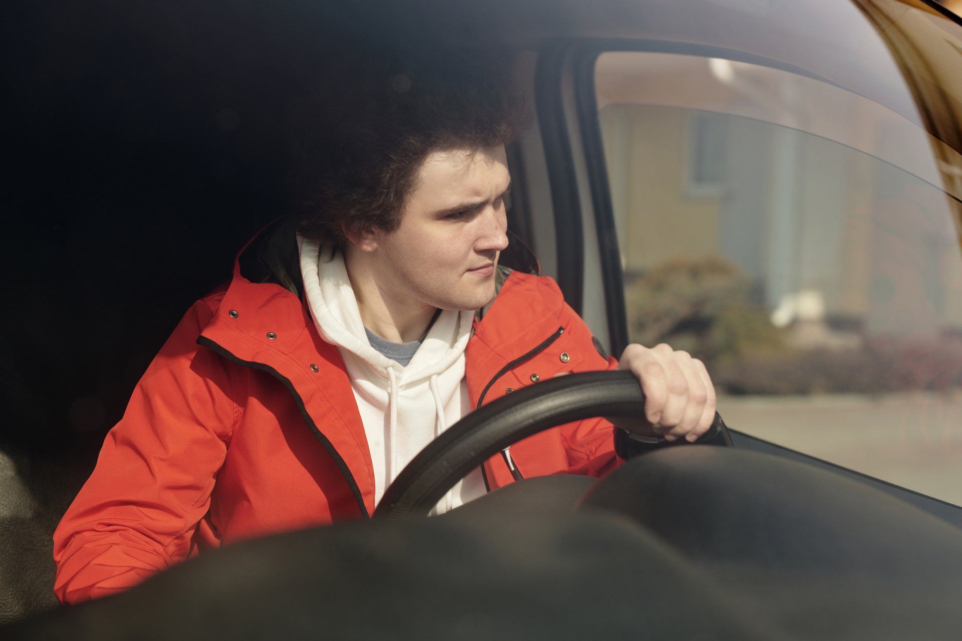 A man in a red jacket is driving a car.