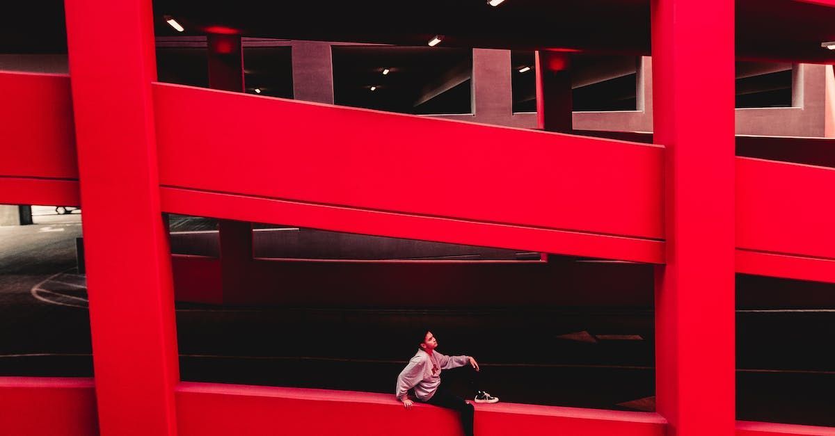 A man is sitting on a red wall in a parking garage.