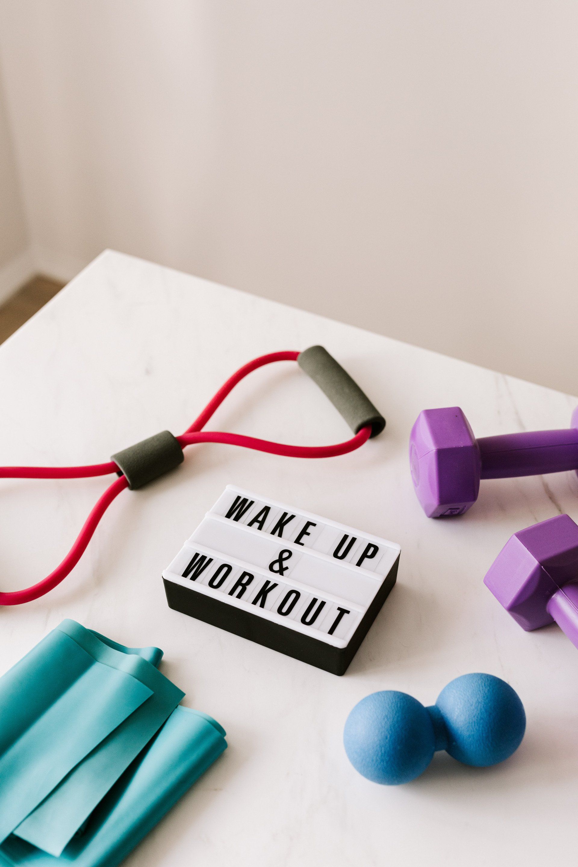 The photo captures a stretch band, a pair of weights, a stress ball, and an elastic band arranged around a small sign that reads 
