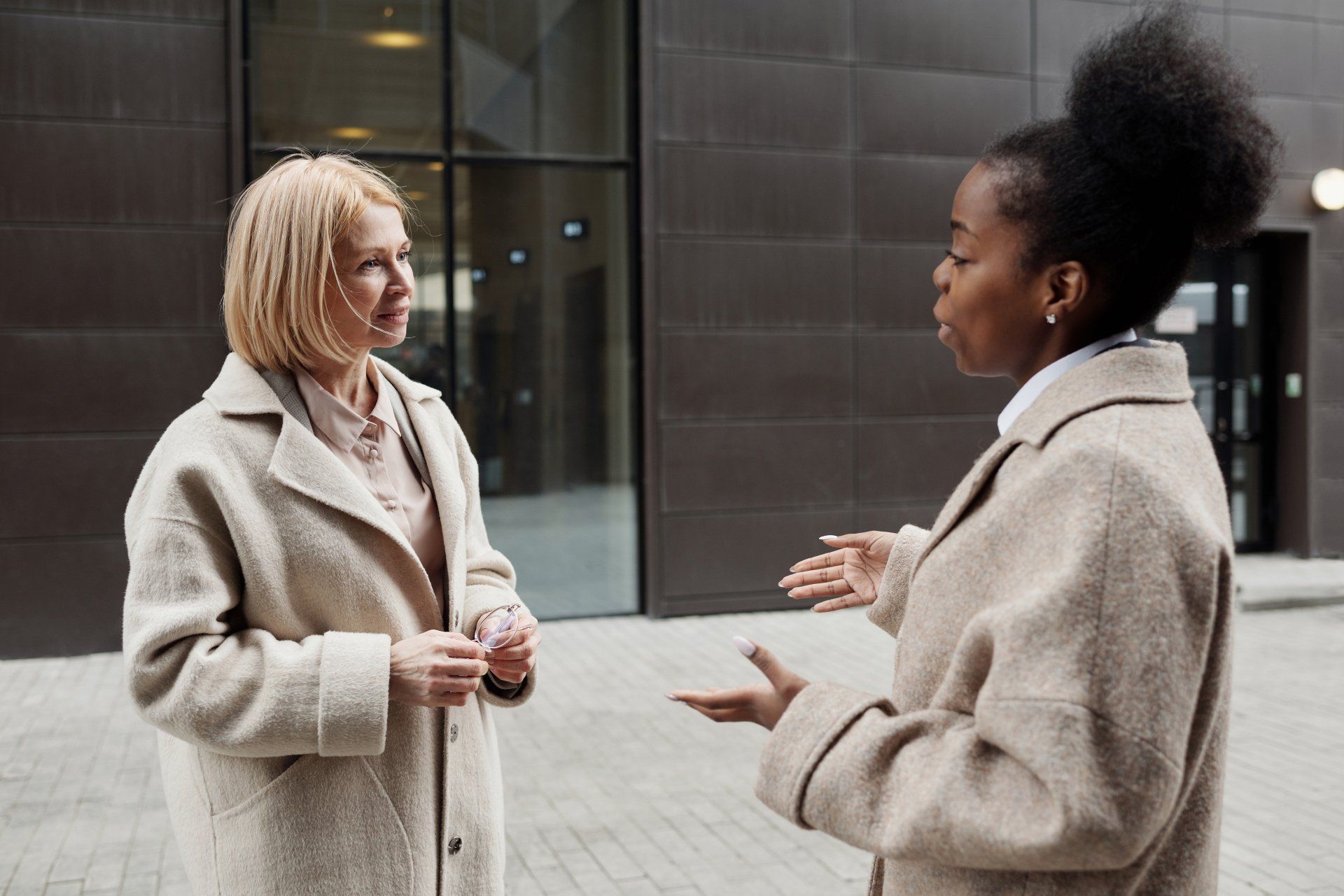 Two women are conversing in front of a building.