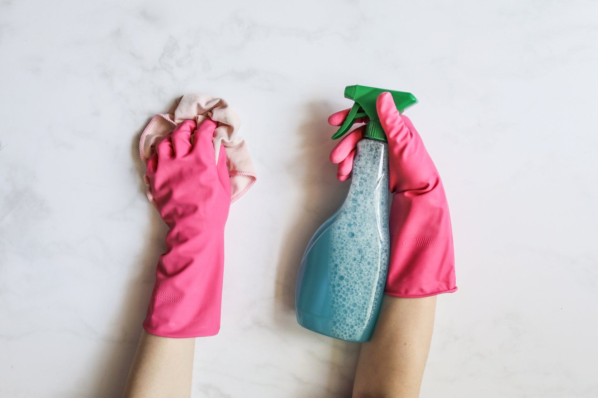 a person wearing pink gloves is holding a spray bottle and a cloth .