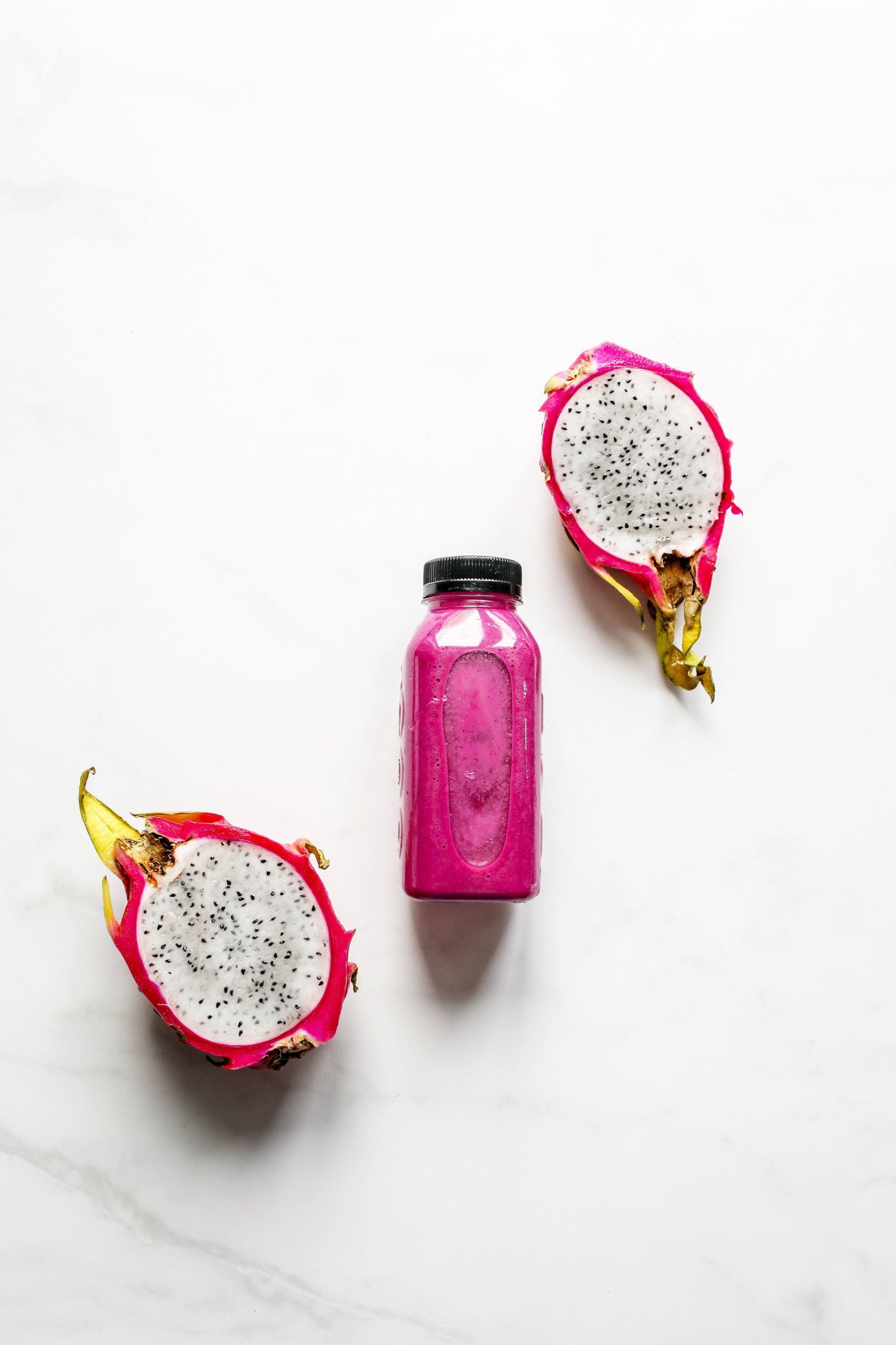 Two dragon fruits and a bottle of dragon fruit juice on a white surface.