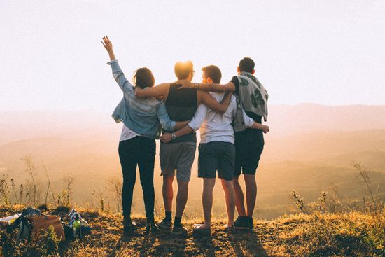 A group of people are standing on top of a hill with their arms around each other.