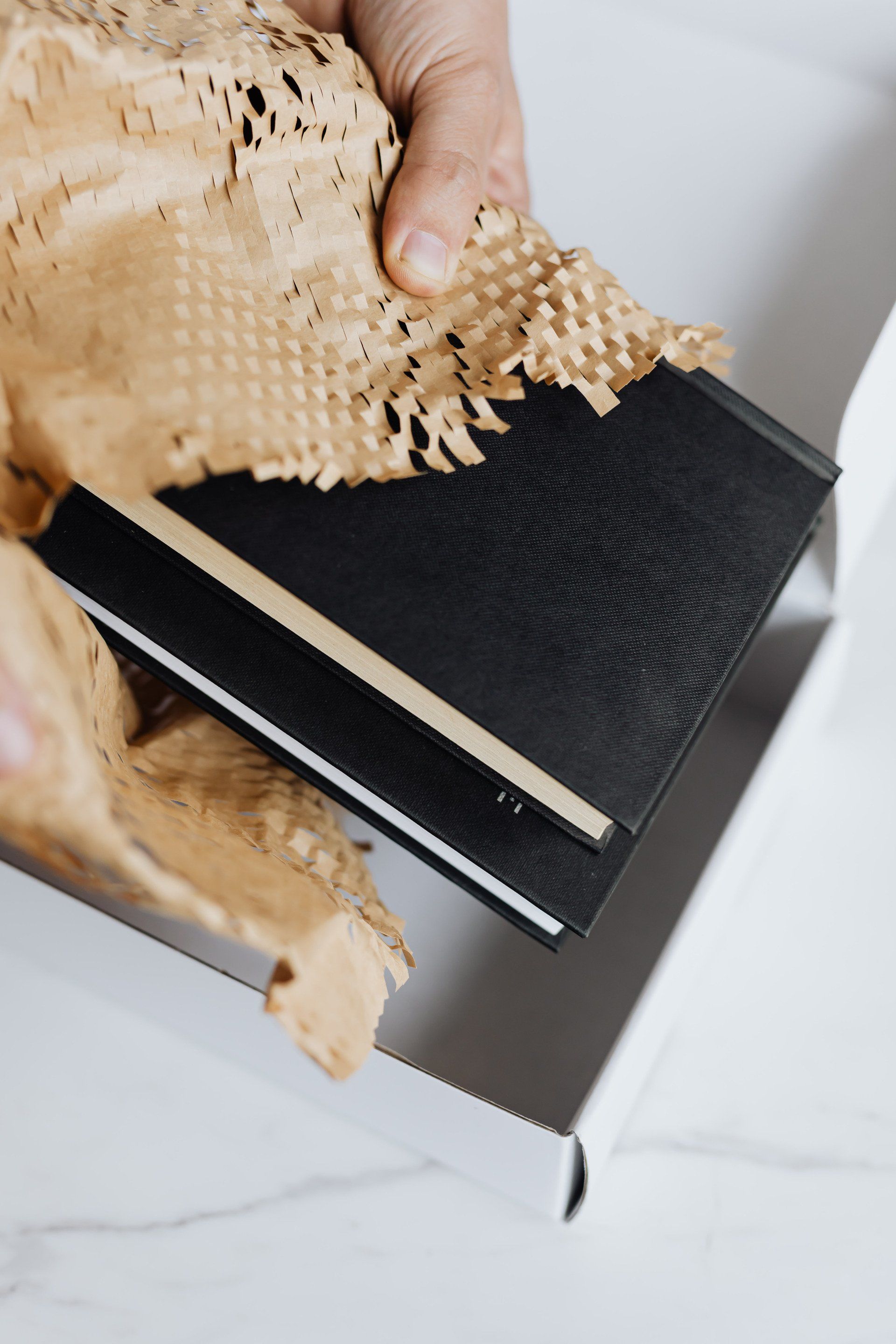 A person is wrapping a book in brown paper and putting it in a box.