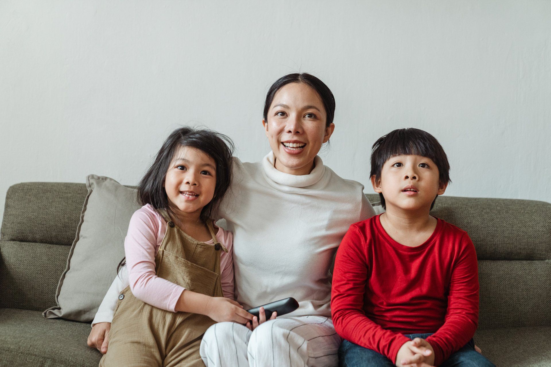 A woman and two children are sitting on a couch watching tv.
