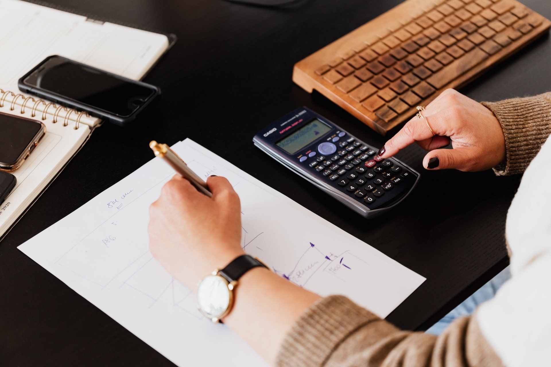 a person is using a calculator and writing on a piece of paper .