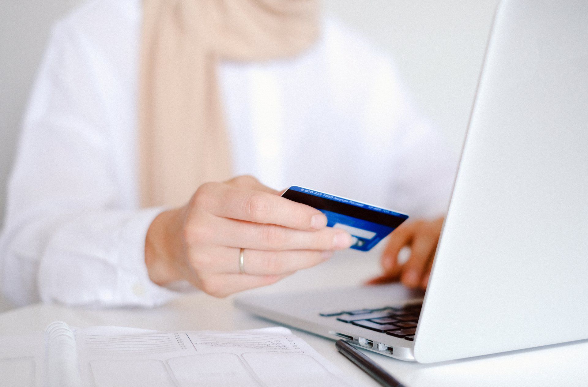 A person holding a credit card in front of their laptop while they online shop.