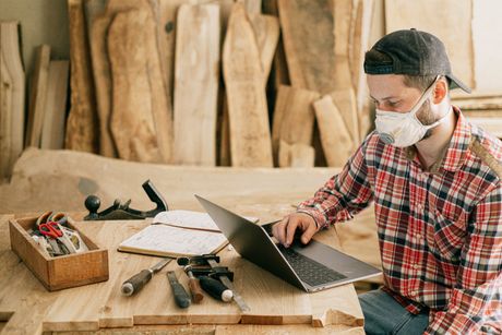 A man wearing a mask is sitting at a table using a laptop computer.