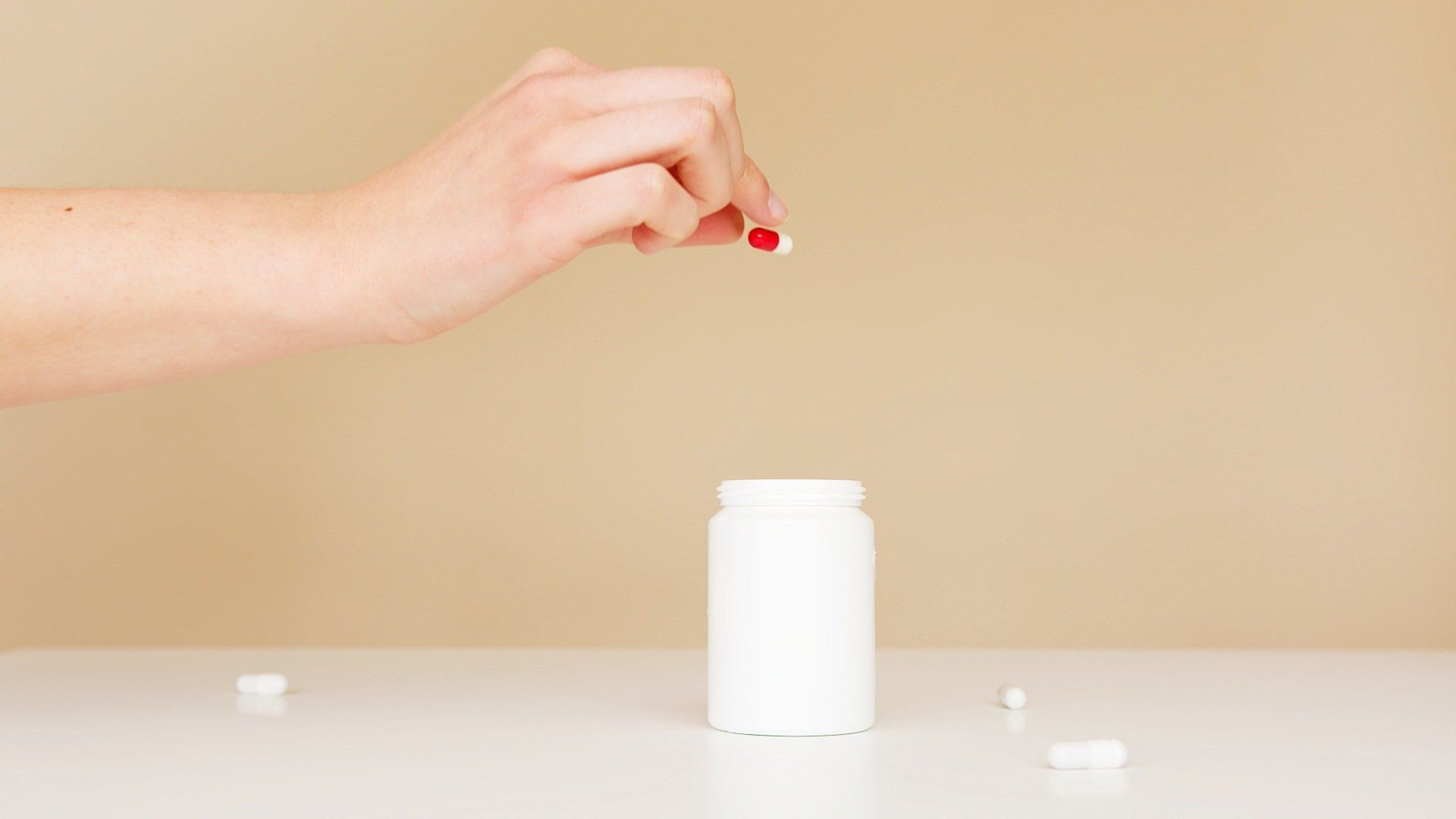 A woman is taking a pill from a bottle on a table.