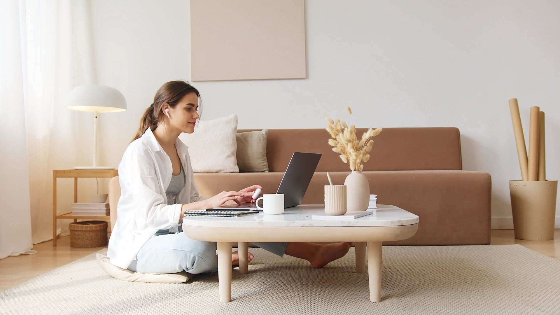a woman is sitting on the floor in front of a couch using a laptop computer to write property descriptions for her new listings.