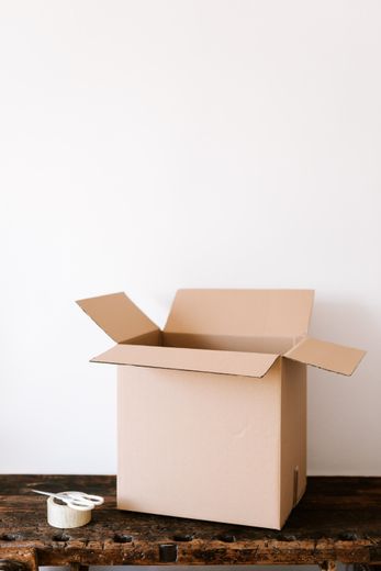 An open cardboard box is sitting on a wooden table next to a roll of tape.