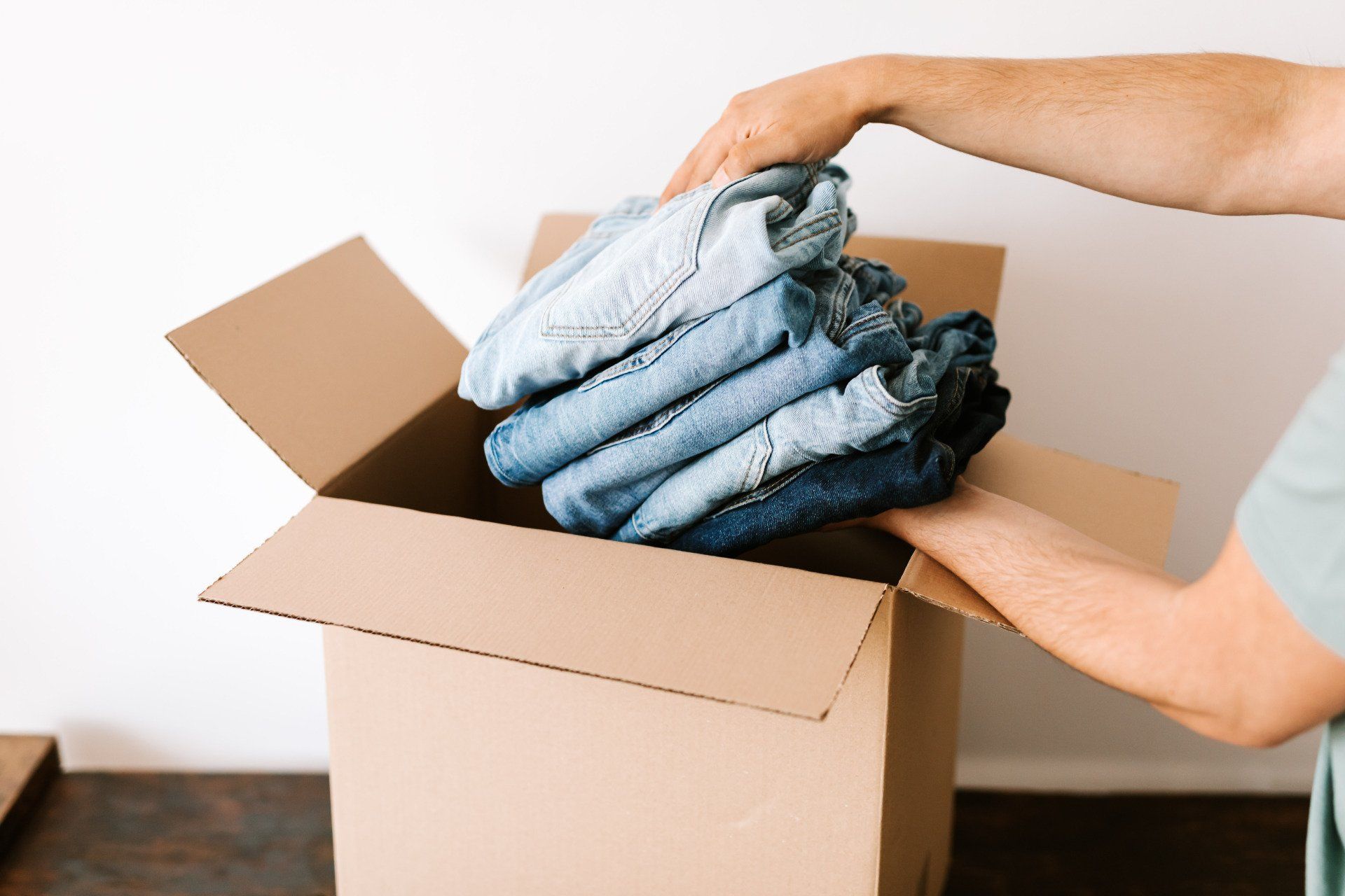 Image of person putting a stack of jeans into a box to donate.