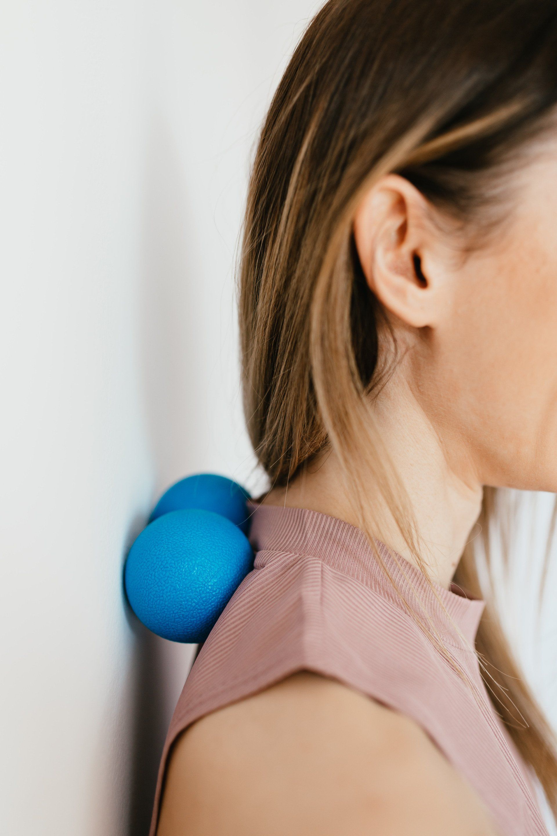 A woman is using a blue ball to massage her neck.