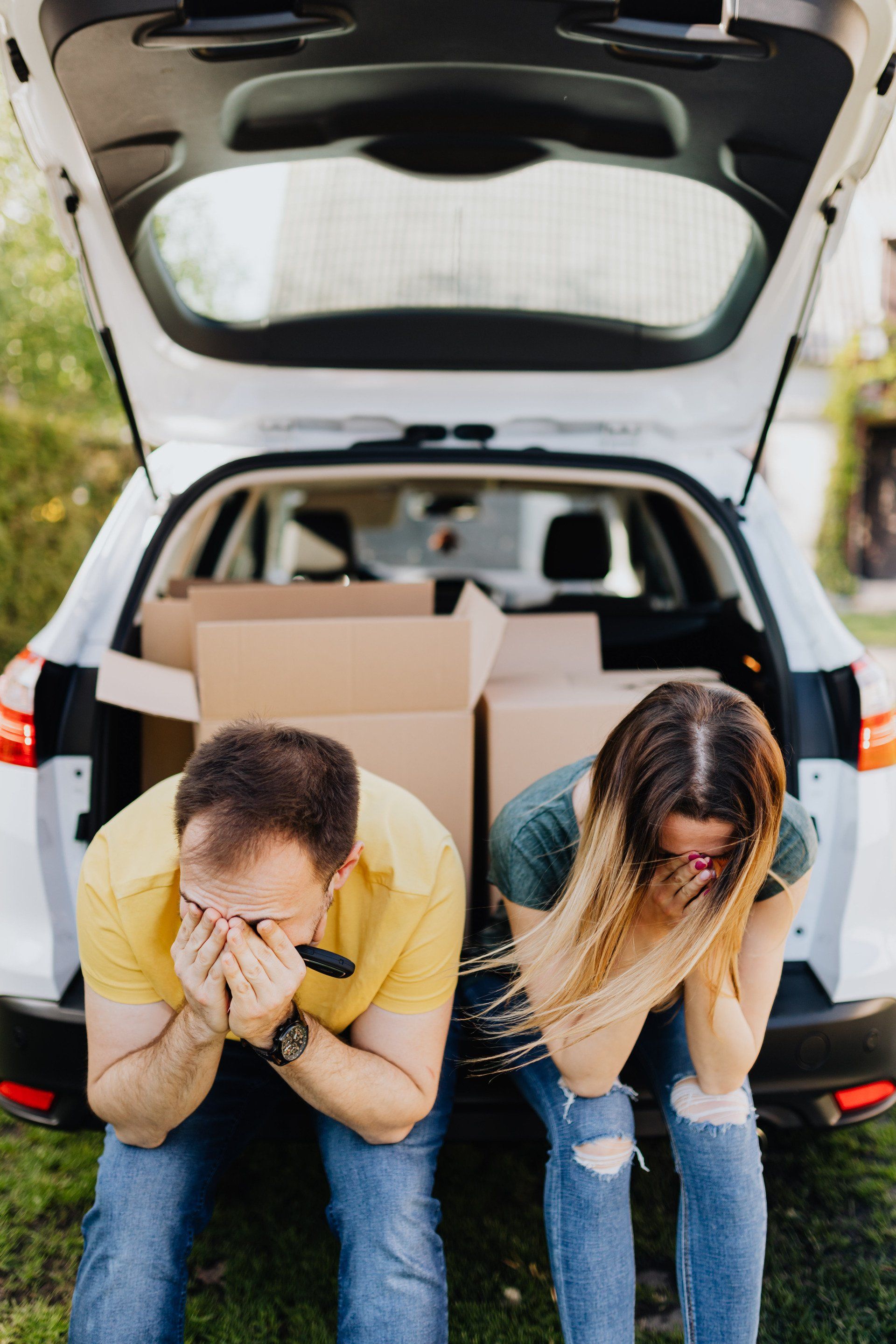 A man and a woman are sitting in the back of a car with boxes in the trunk.