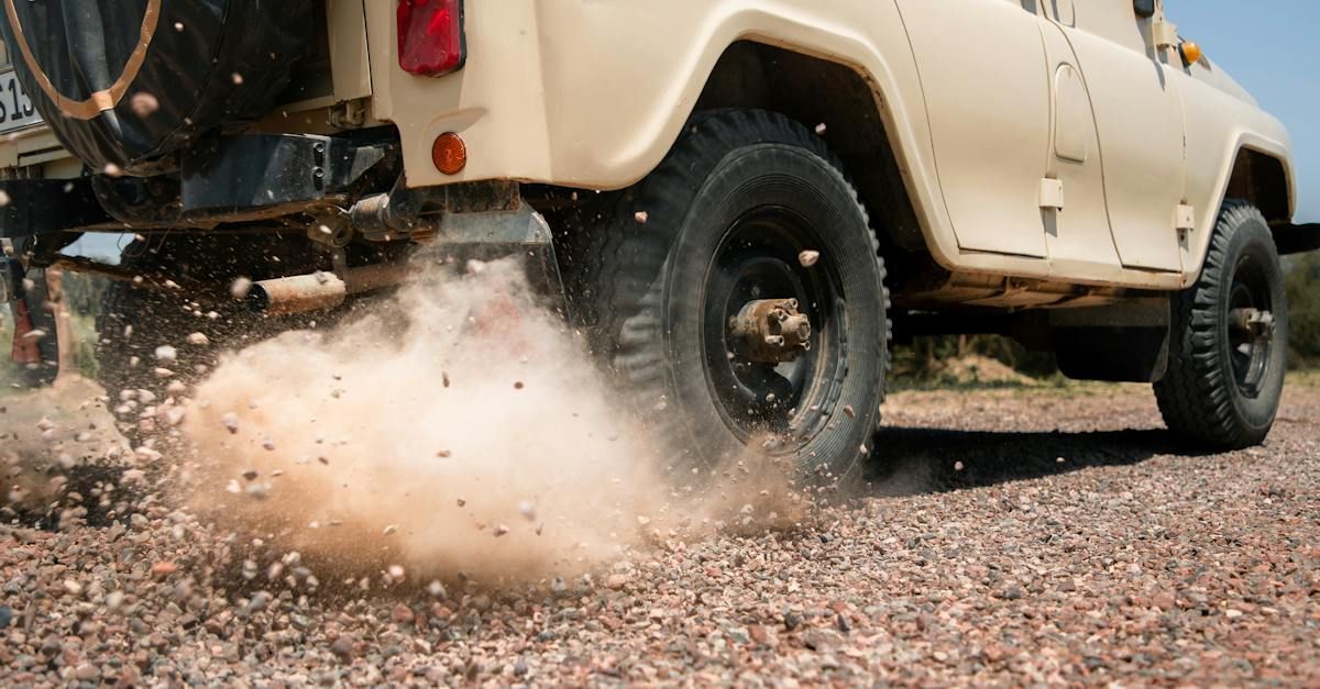 a jeep is driving on a gravel road and kicking up dirt .