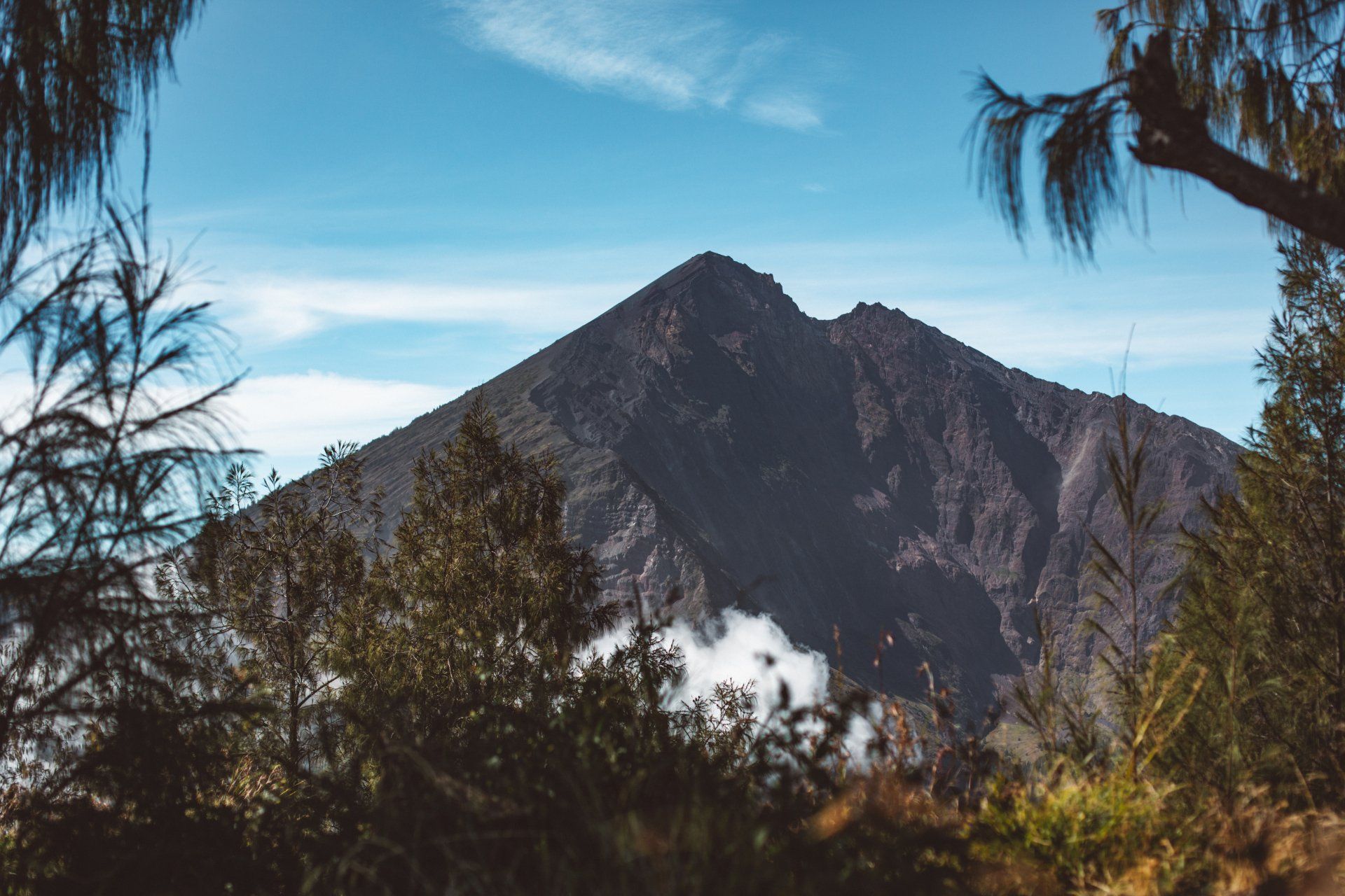 A mountain with trees in the foreground and a blue sky in the background.