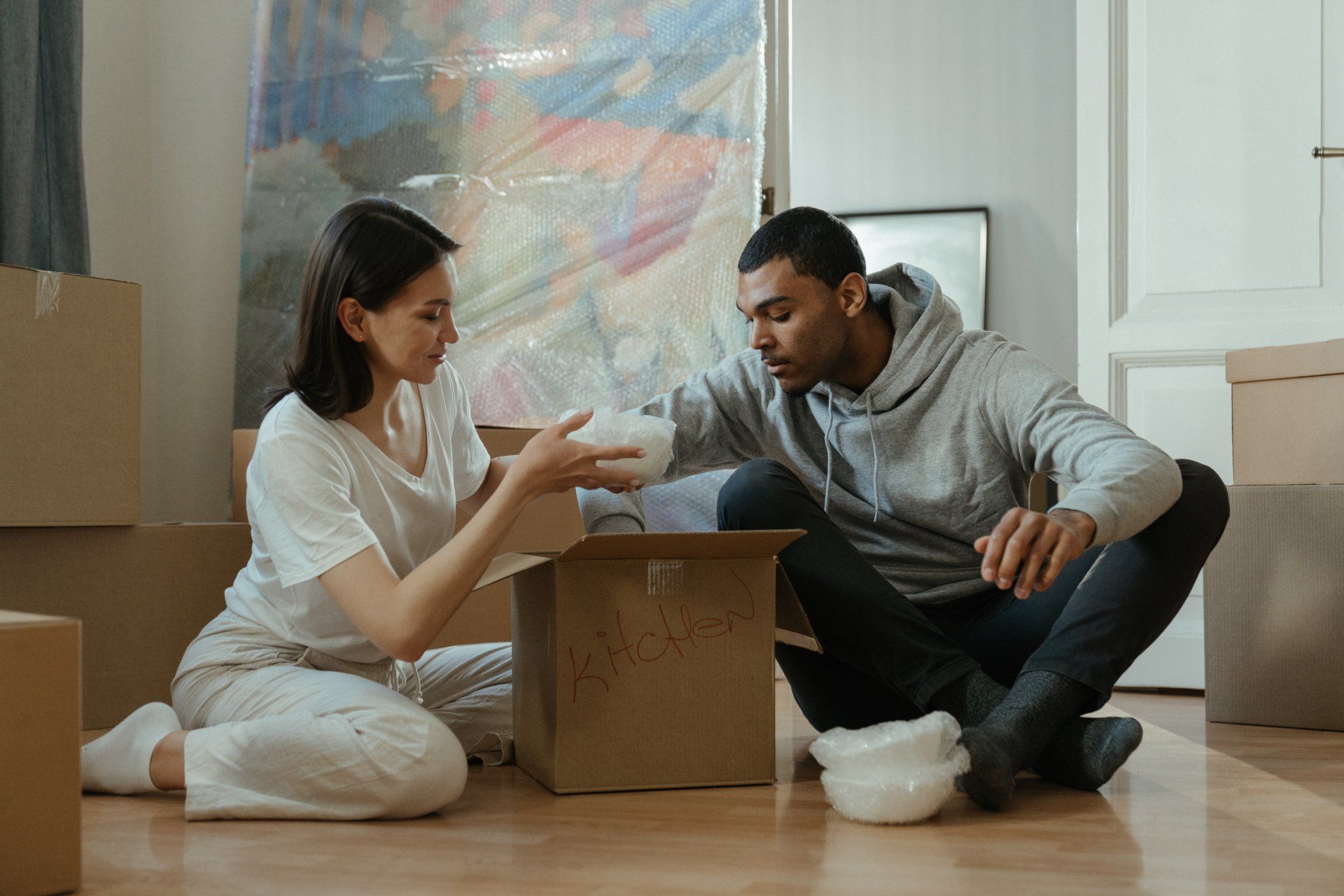 A man and a woman are sitting on the floor surrounded by cardboard boxes.