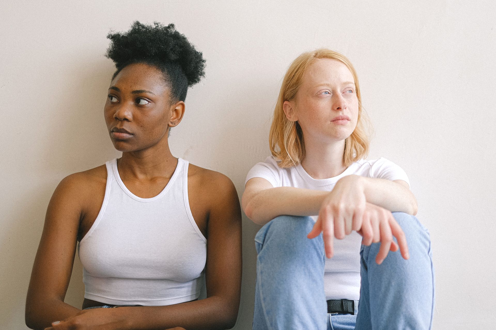 Two women sitting next to each other looking in opposite directions to avoid looking at each other