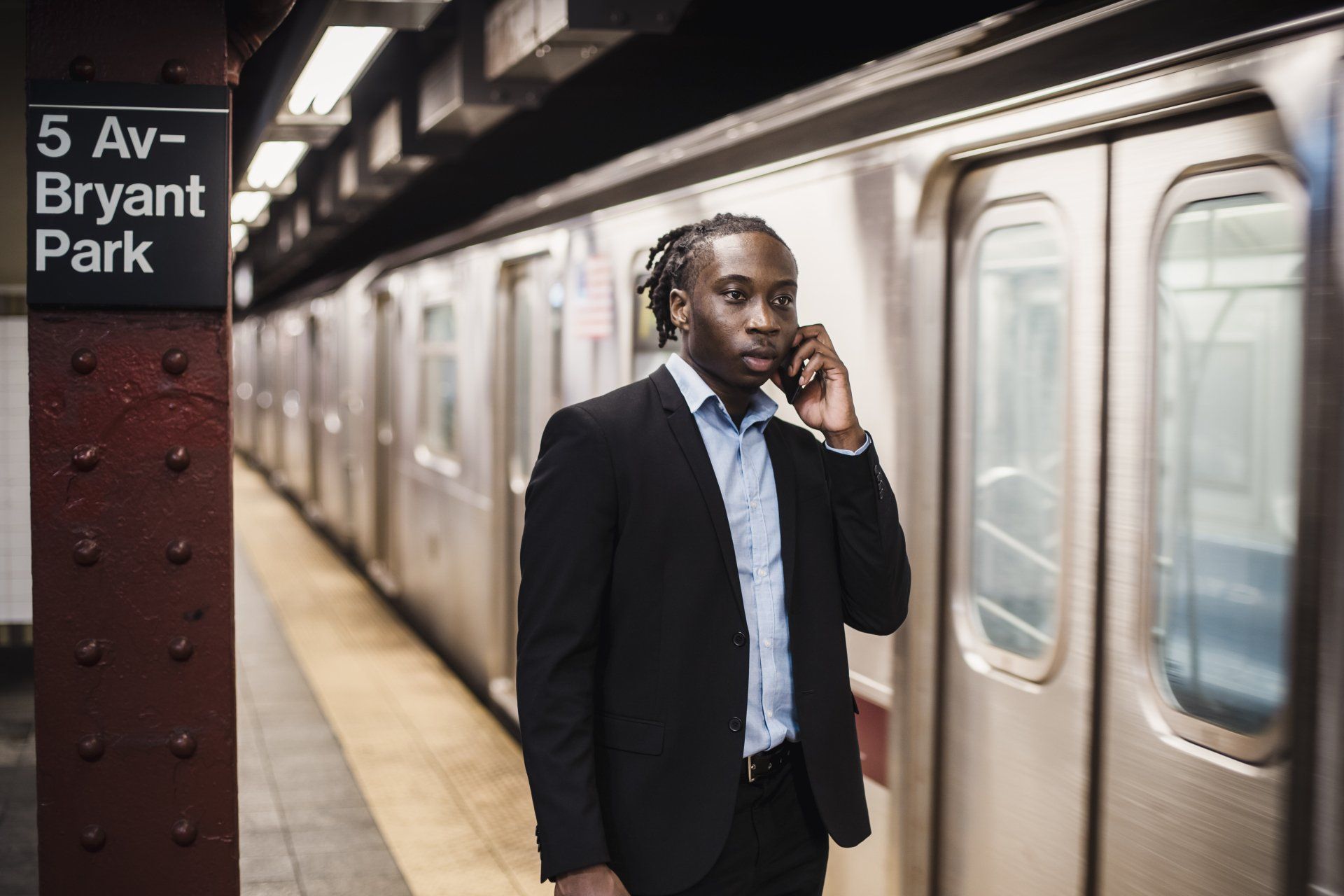 Man in suit talking on phone on subway platform near train.