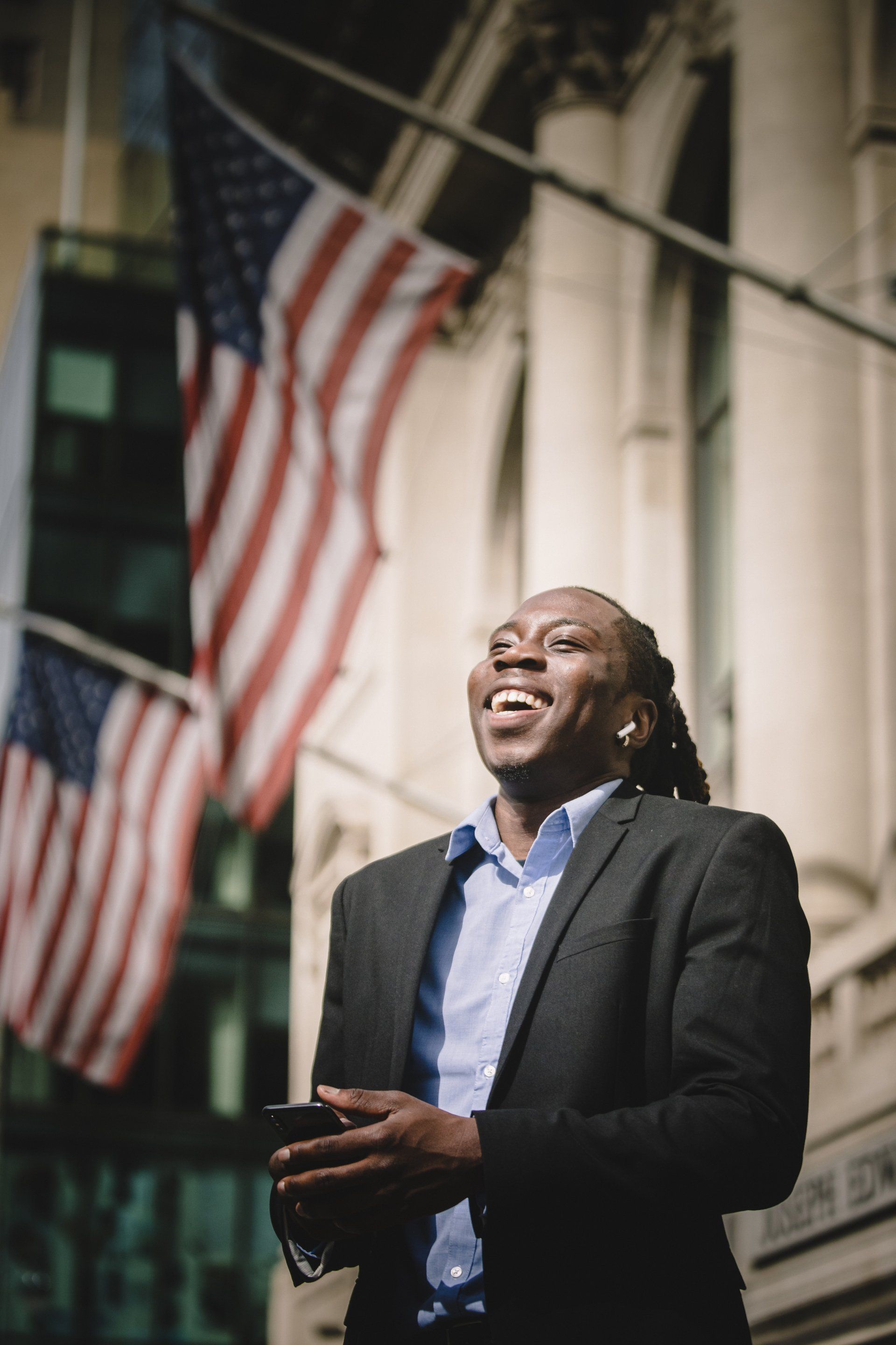 A man in a suit is standing in front of an american flag holding a cell phone.