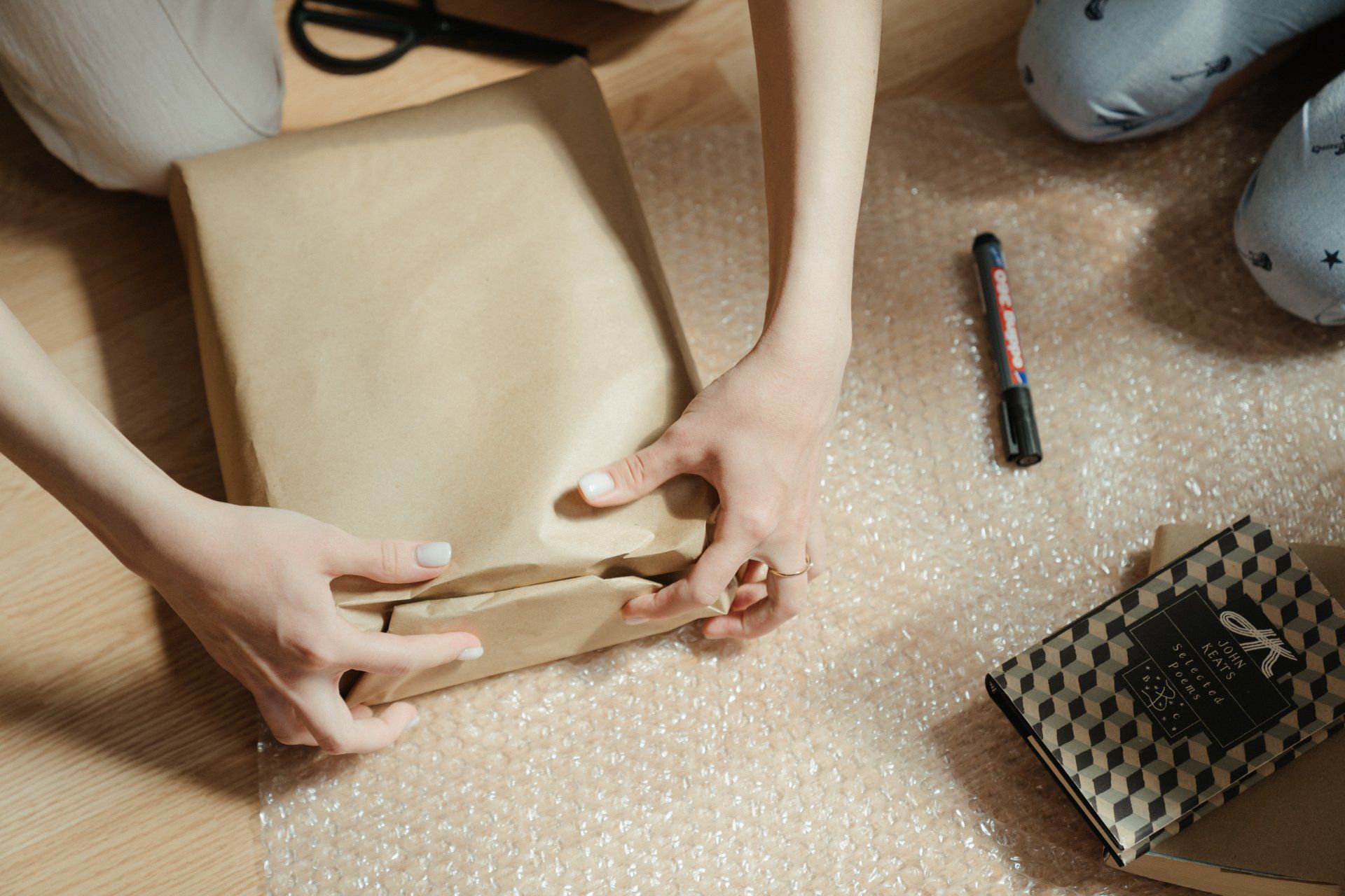 A person is wrapping a package in brown paper on the floor.