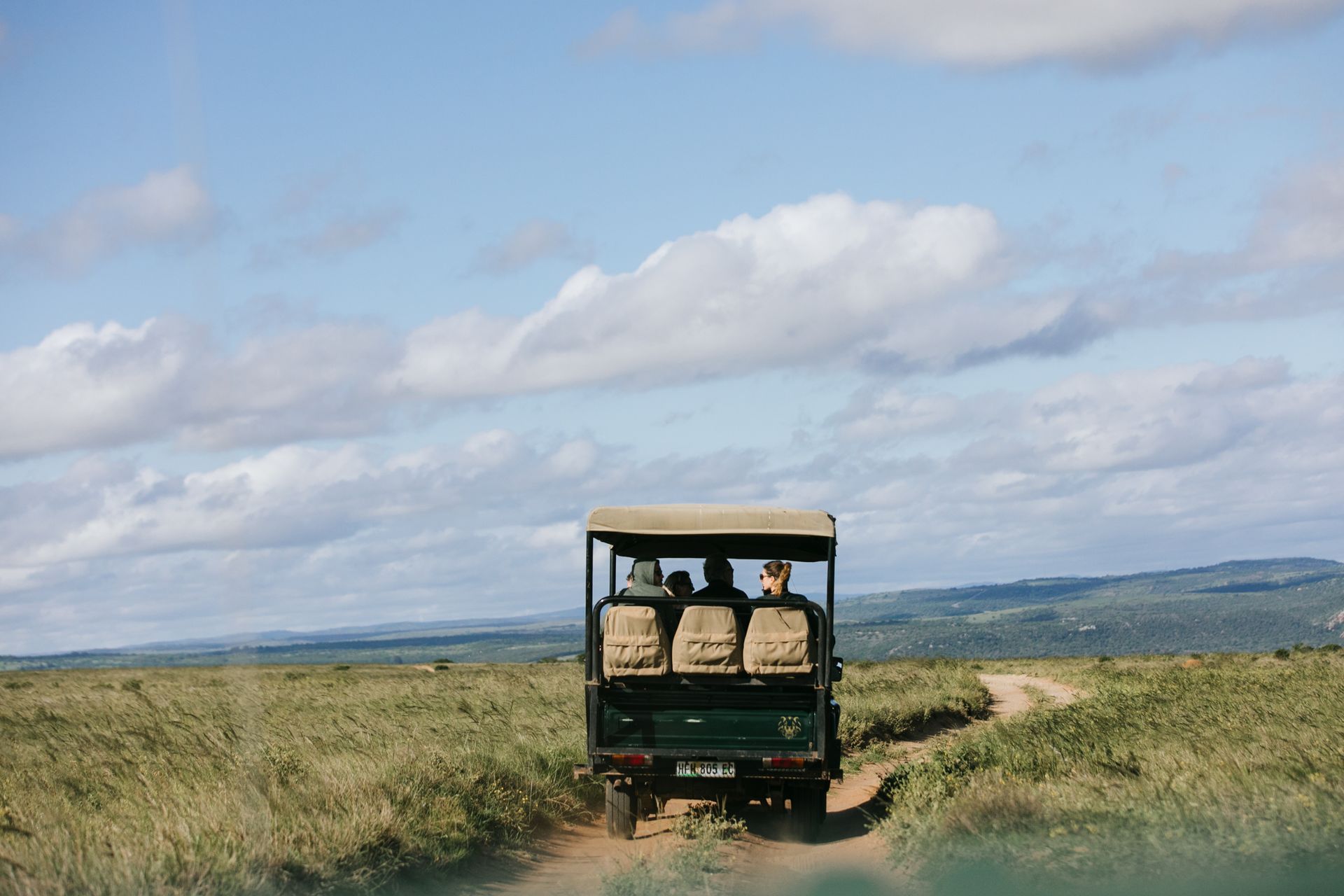 A jeep is driving down a dirt road through a grassy field.