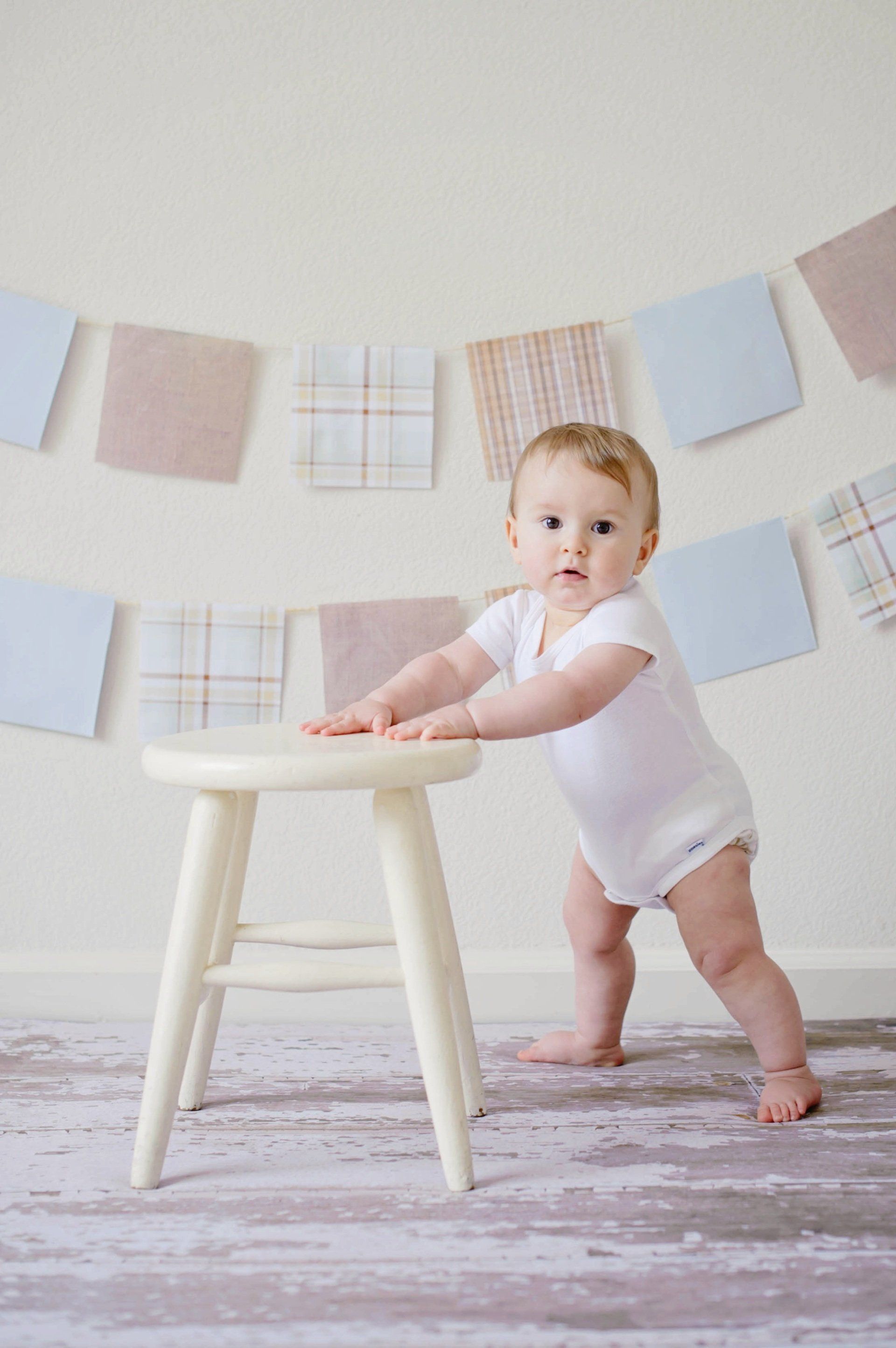 baby standing with hands on stool