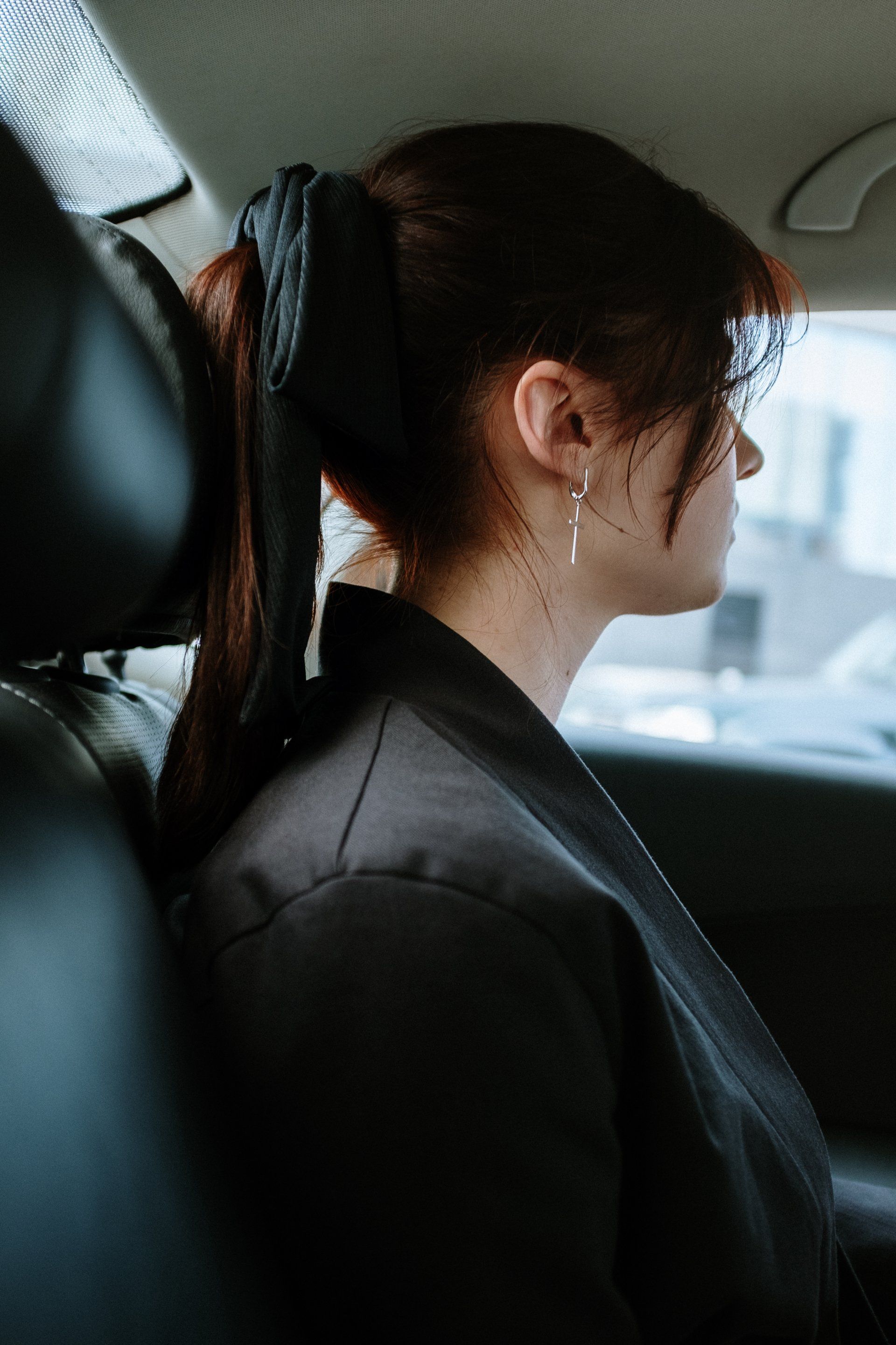 A woman is sitting in the back seat of a car with her hair in a ponytail.