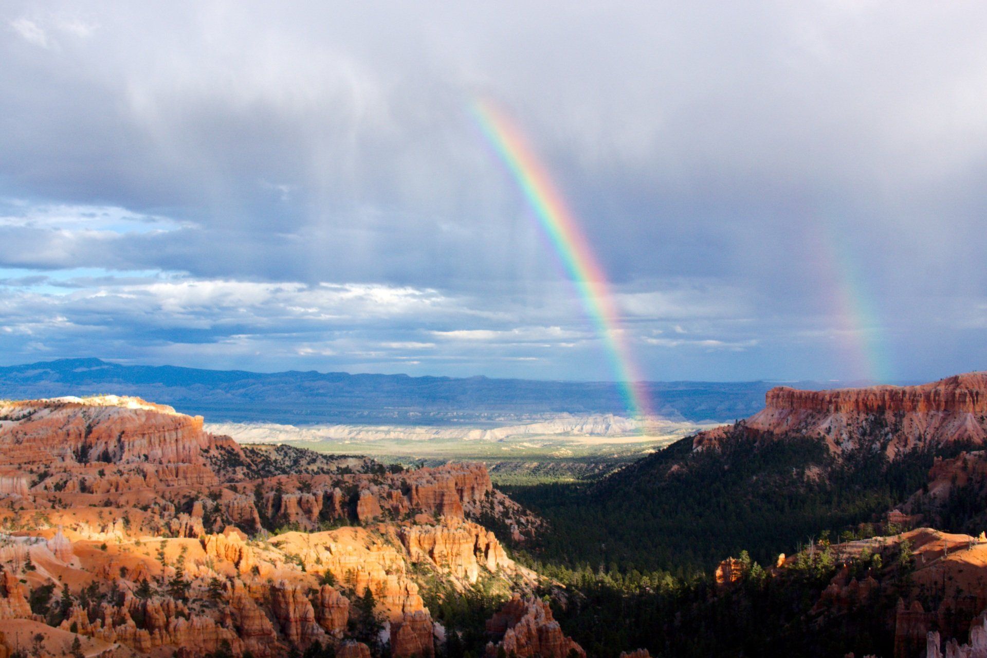There is a double rainbow in the sky over a canyon.