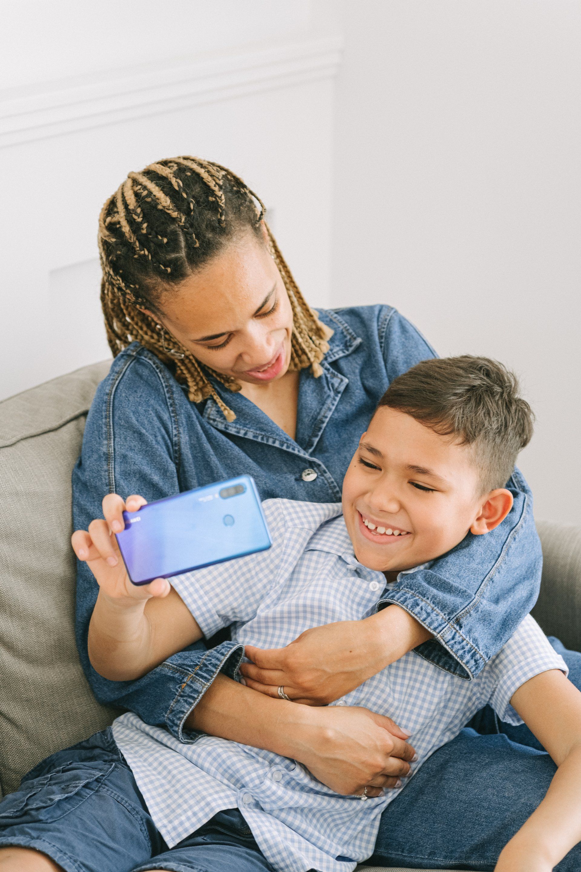 A mom and son are sitting on a couch looking at a cell phone.