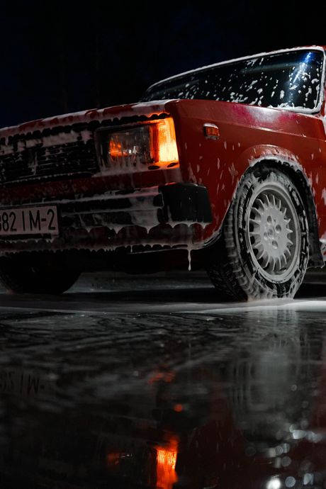 A red car is driving down a wet road at night.