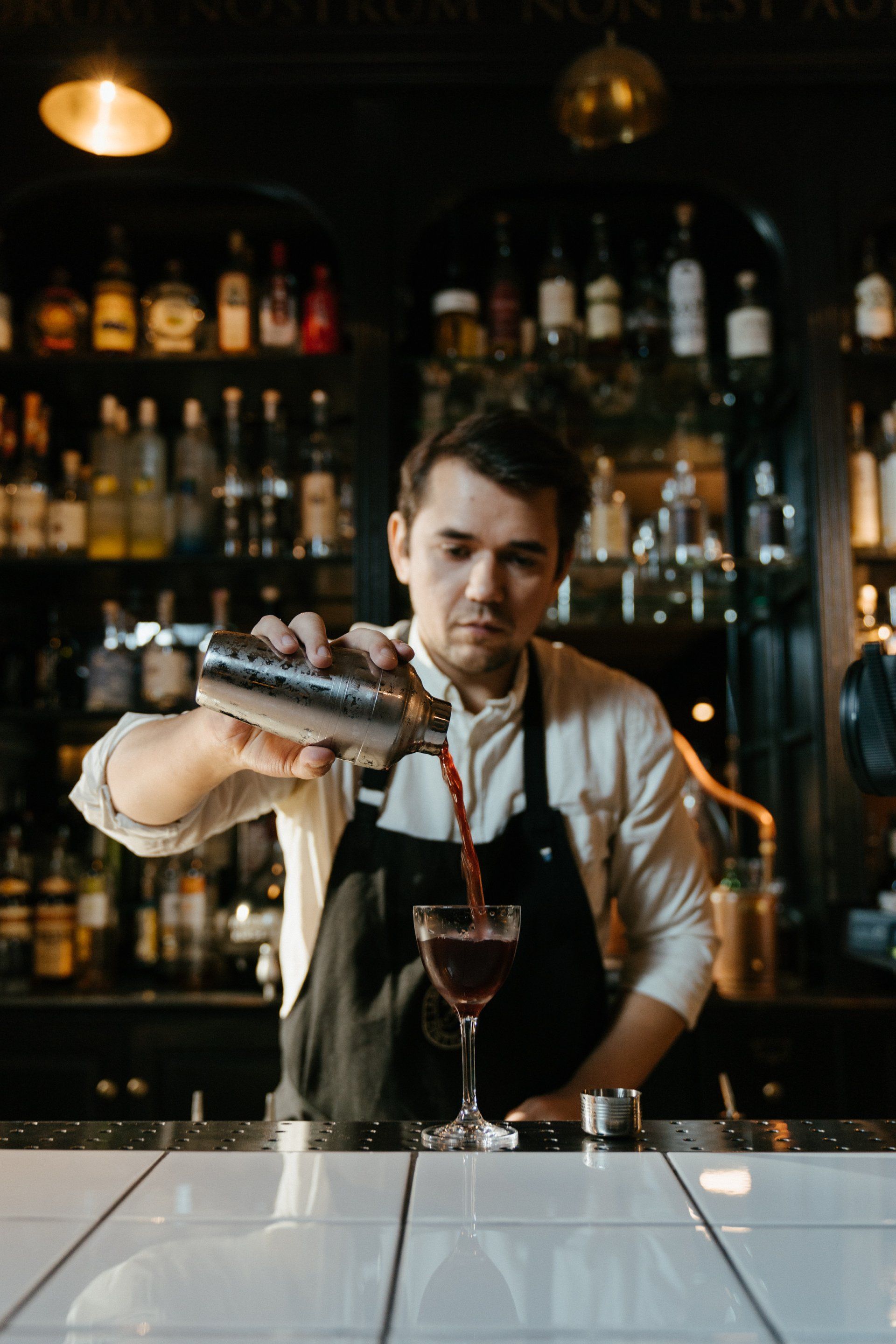 A bartender is pouring a drink into a glass at a bar.