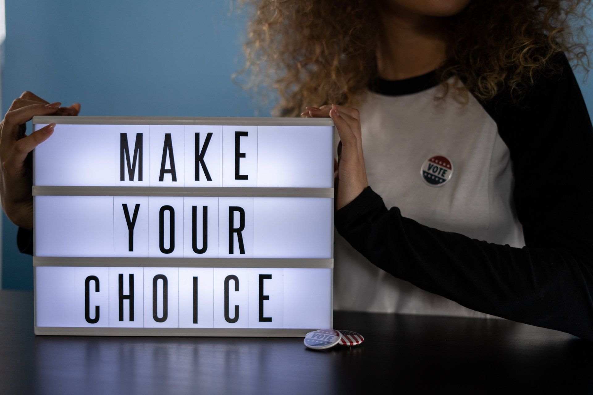 female youth wearing a vote pin behind a sign  that says make your choice