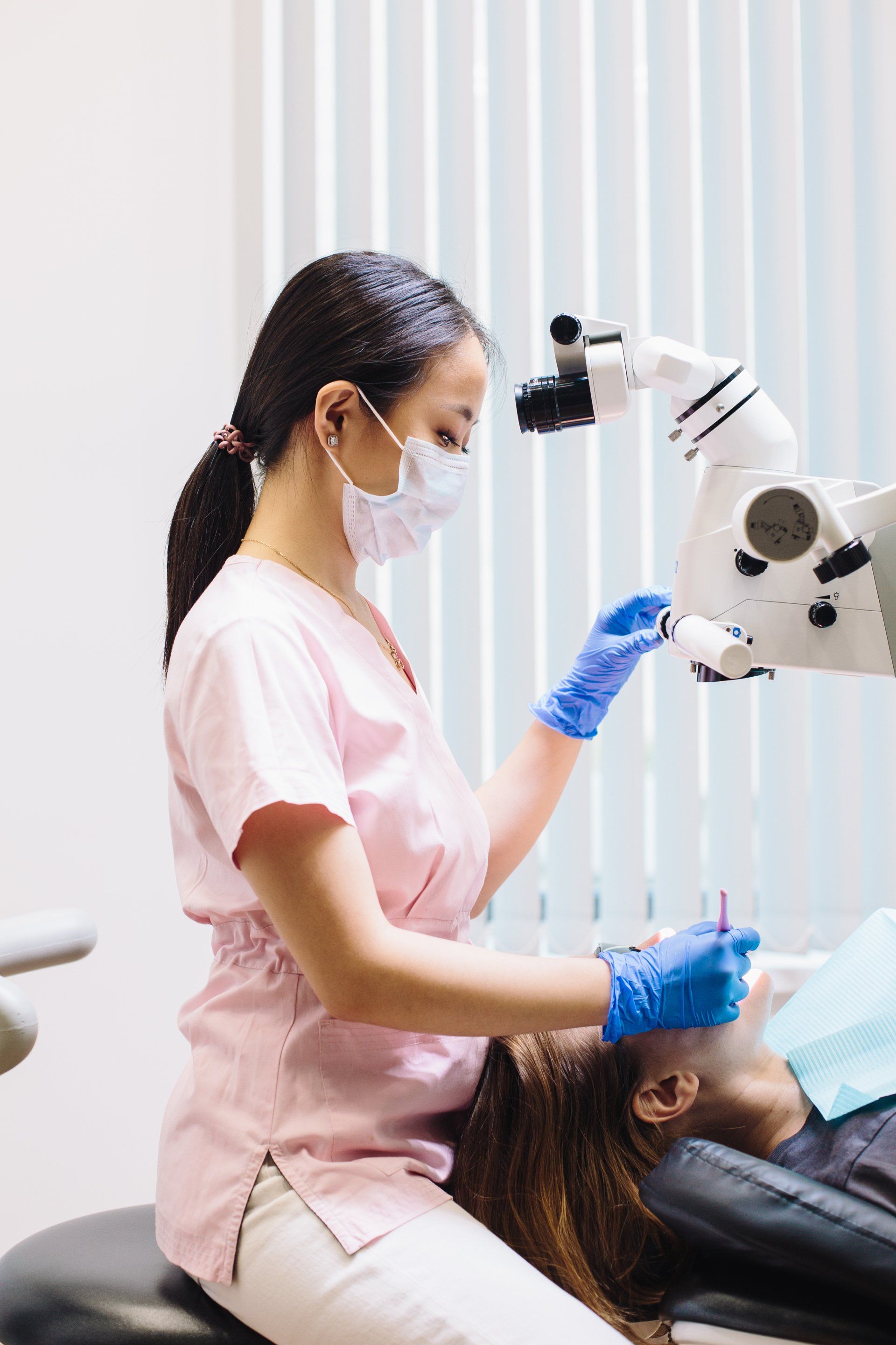 A female dentist is examining a patient 's teeth with a microscope.