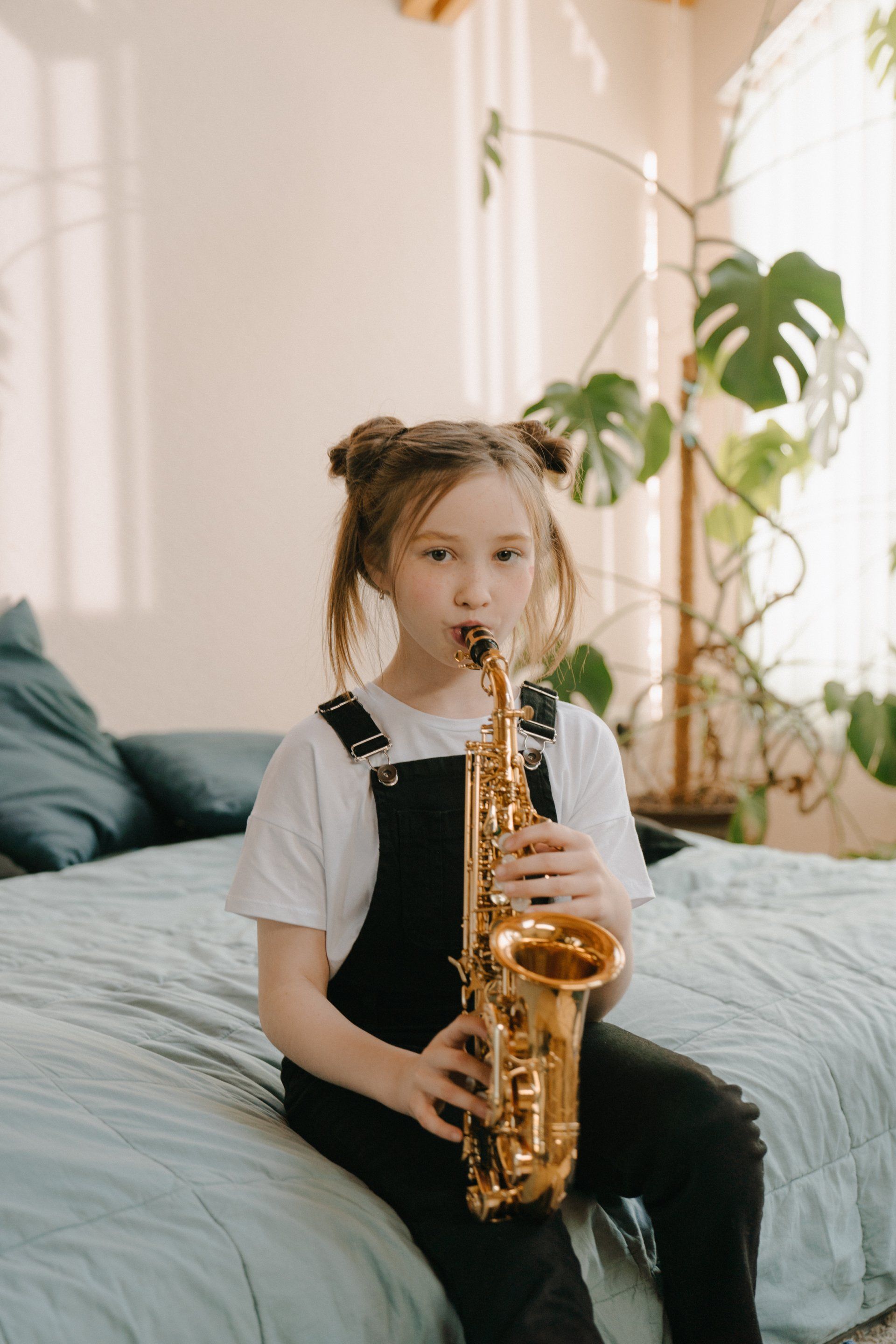 a little girl is sitting on a bed playing a saxophone .