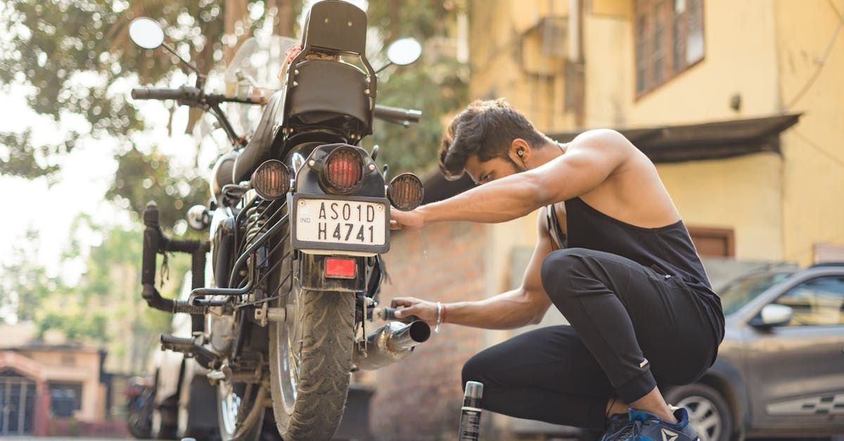 A man is kneeling down next to a motorcycle on the side of the road.