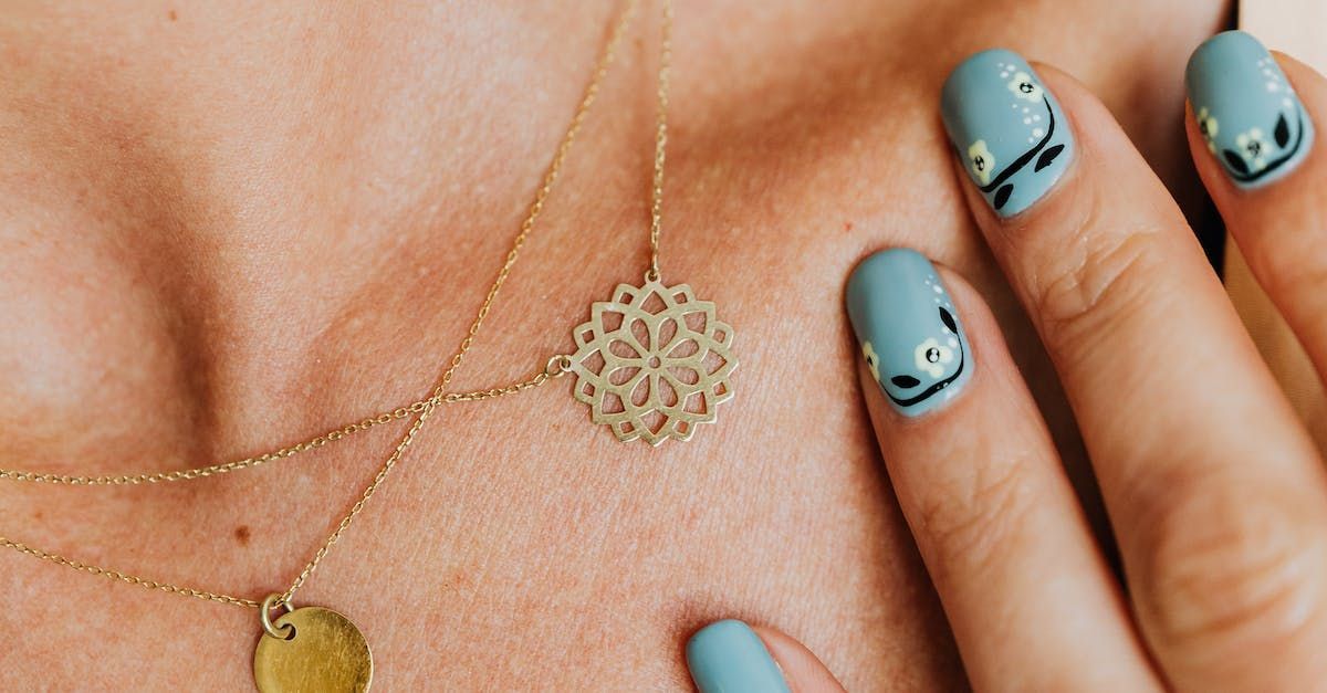 A close up of a woman 's neck with a necklace and blue nails.