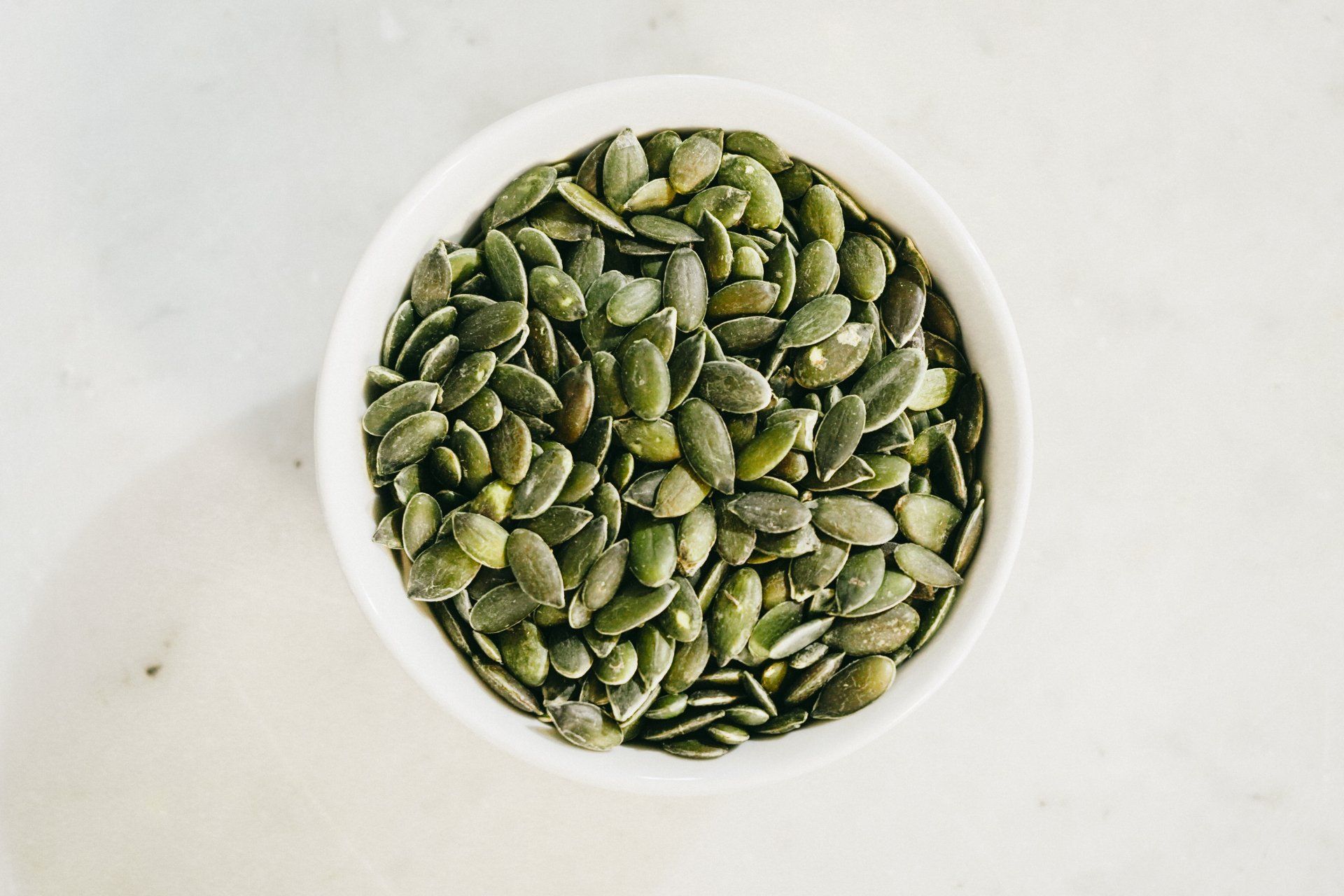 a white bowl filled with green pumpkin seeds on a table .