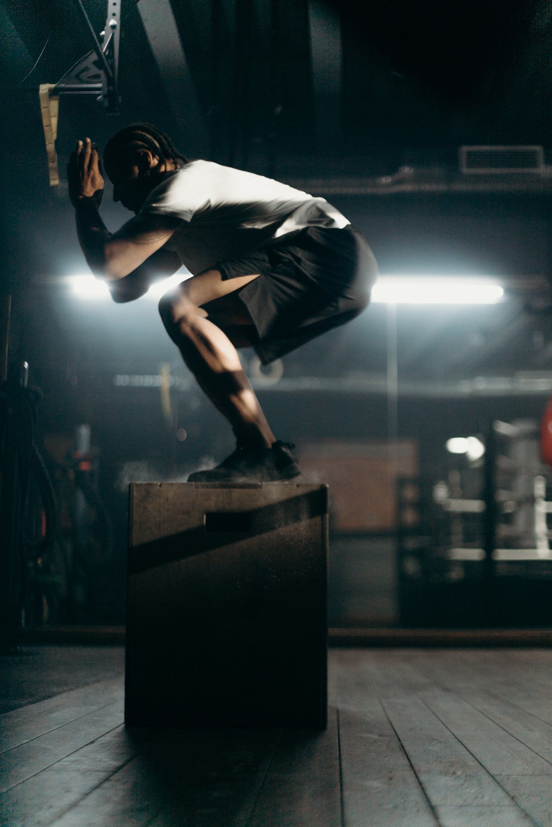 A man is squatting on a wooden box in a gym.
