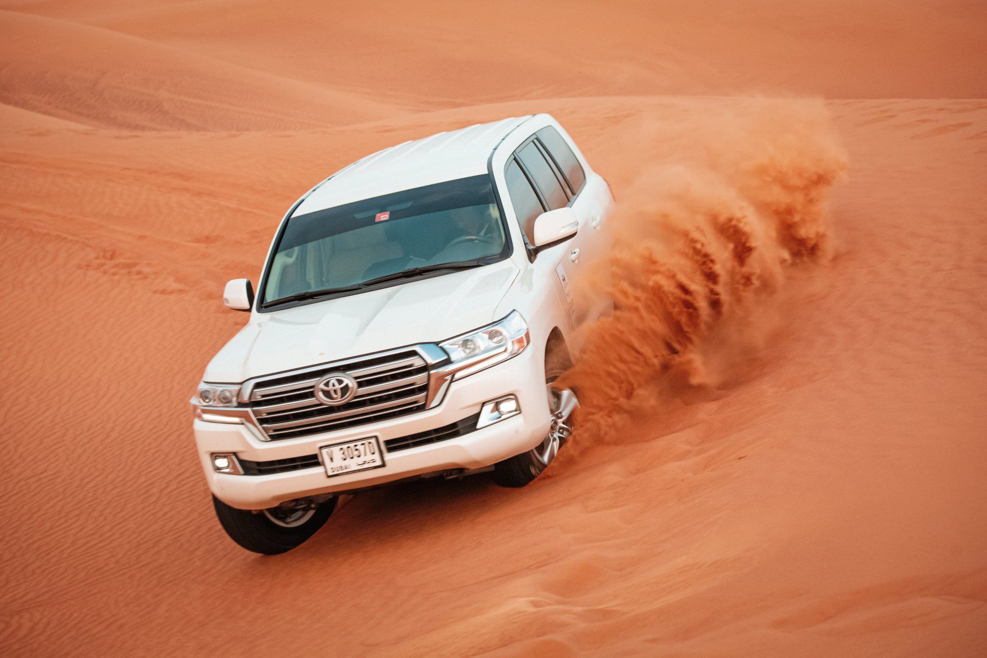 A white suv is driving down a sand dune in the desert.