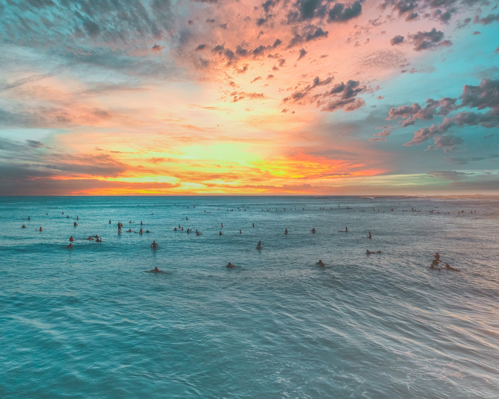 A group of people are swimming in the ocean at sunset.