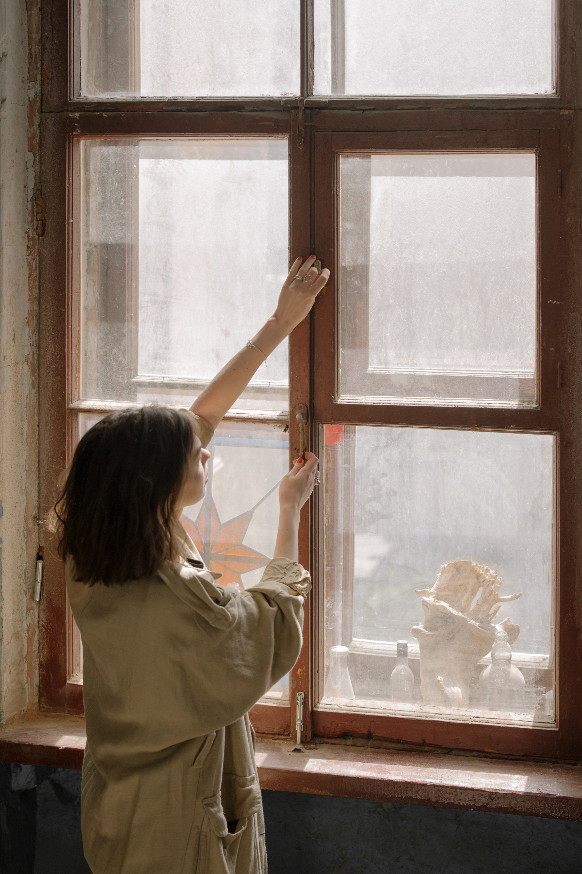 A woman standing in front of a window about to open it.
