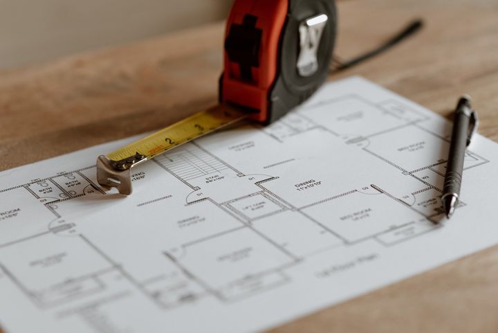 A tape measure is sitting on top of a house plan on a wooden table.