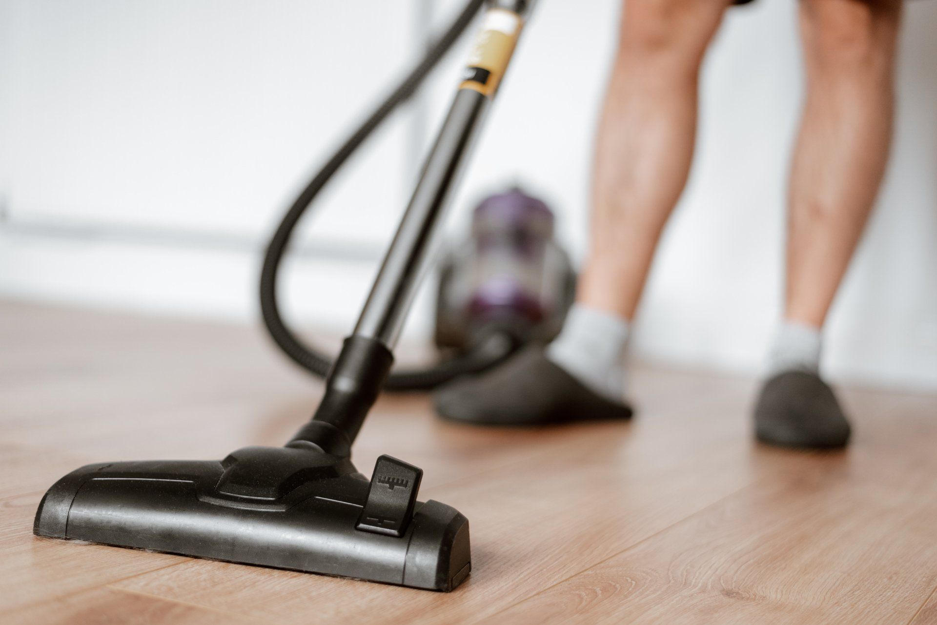 A person using a vacuum cleaner on a hardwood floor to remove dust and debris.
