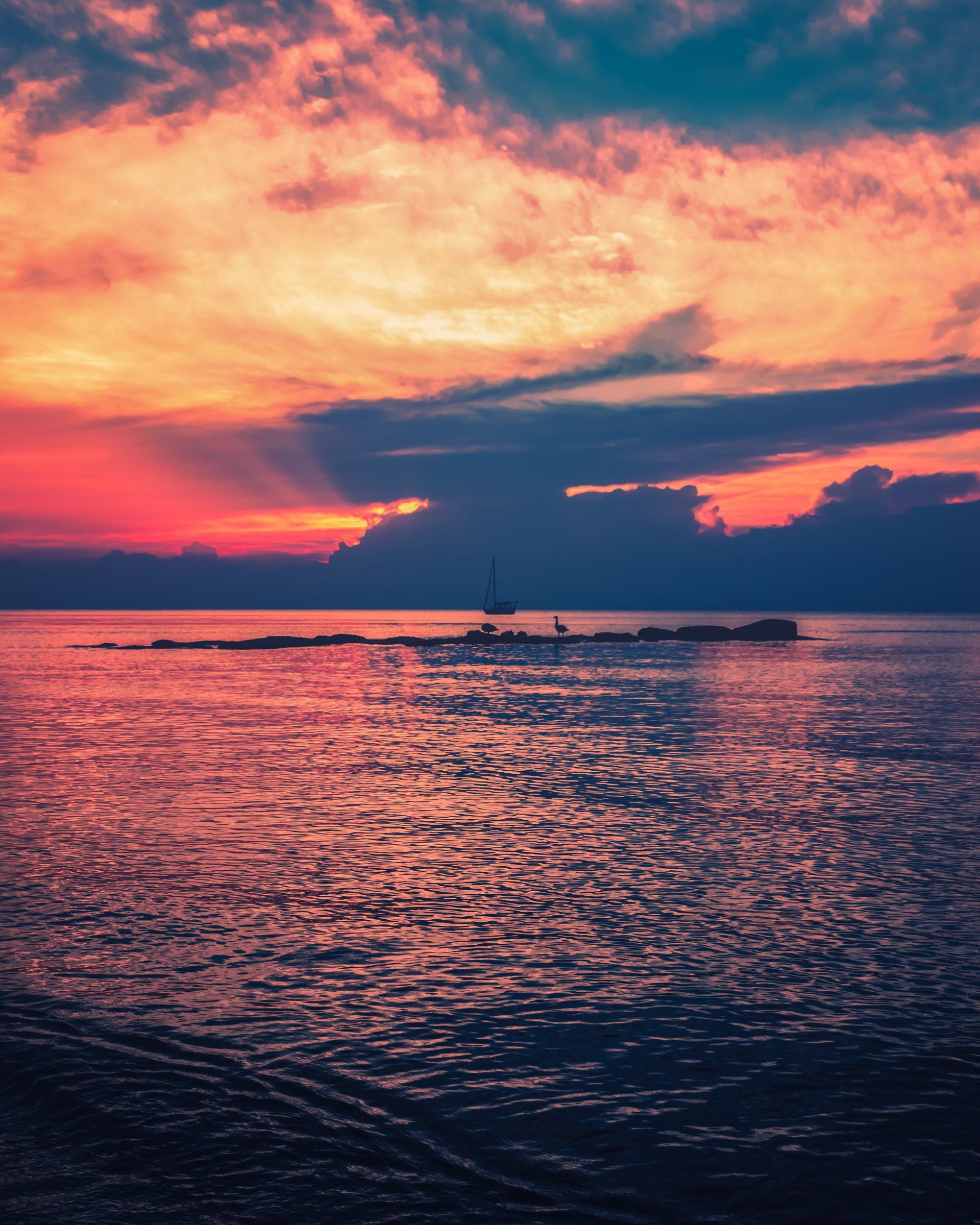 A sunset over the ocean with a boat in the distance.