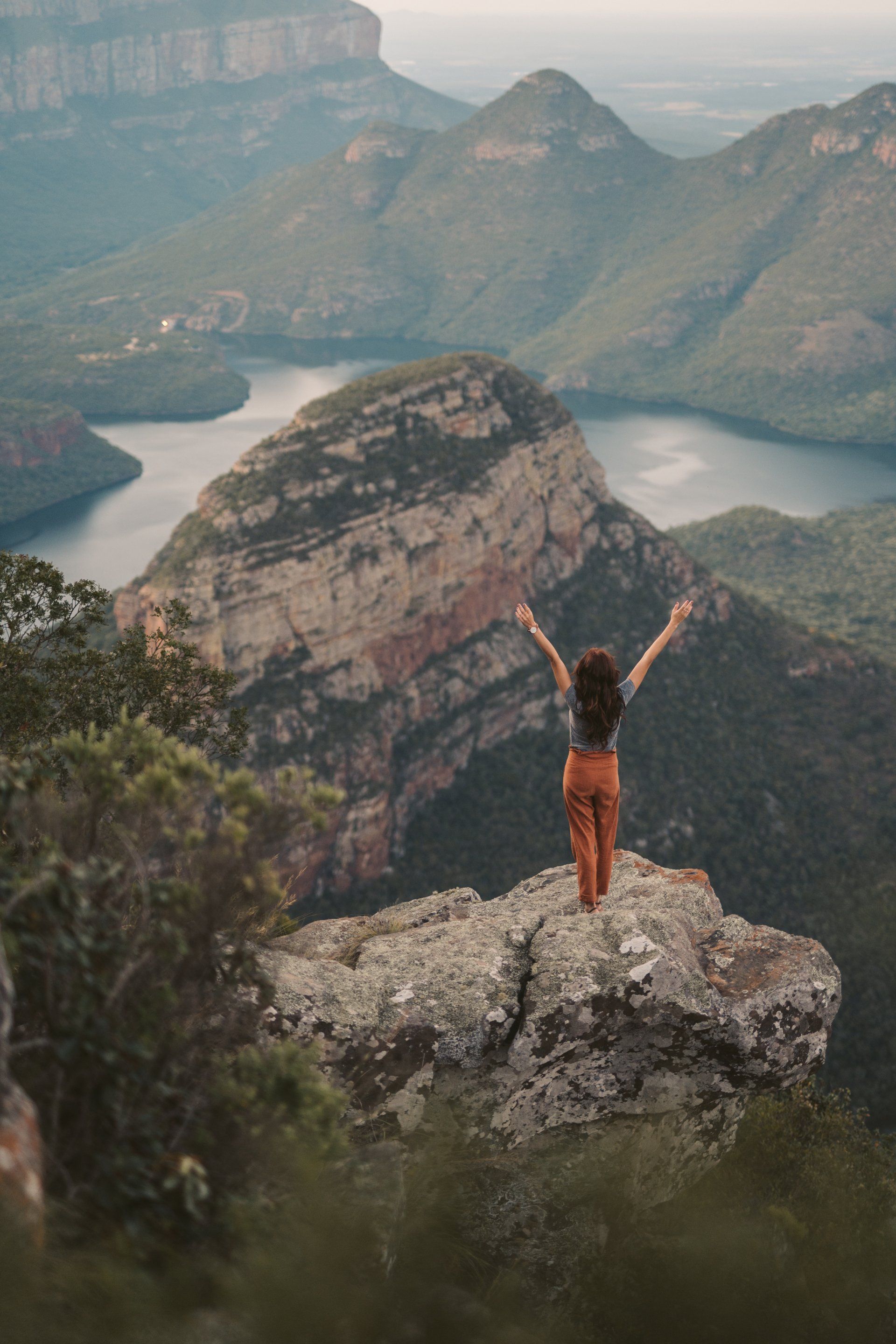 A woman is standing on top of a mountain with her arms outstretched.