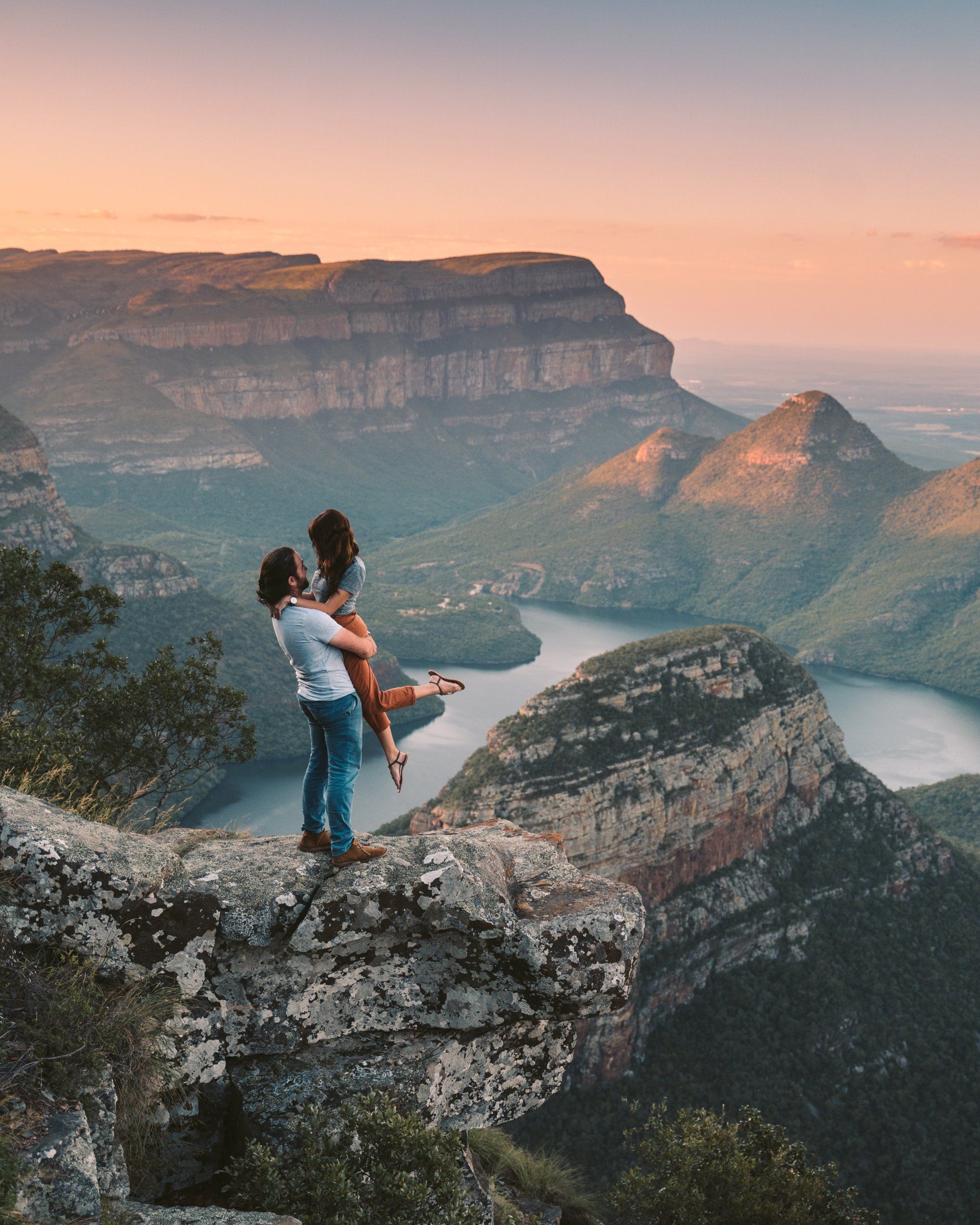 a man is holding a woman in his arms on top of a mountain .