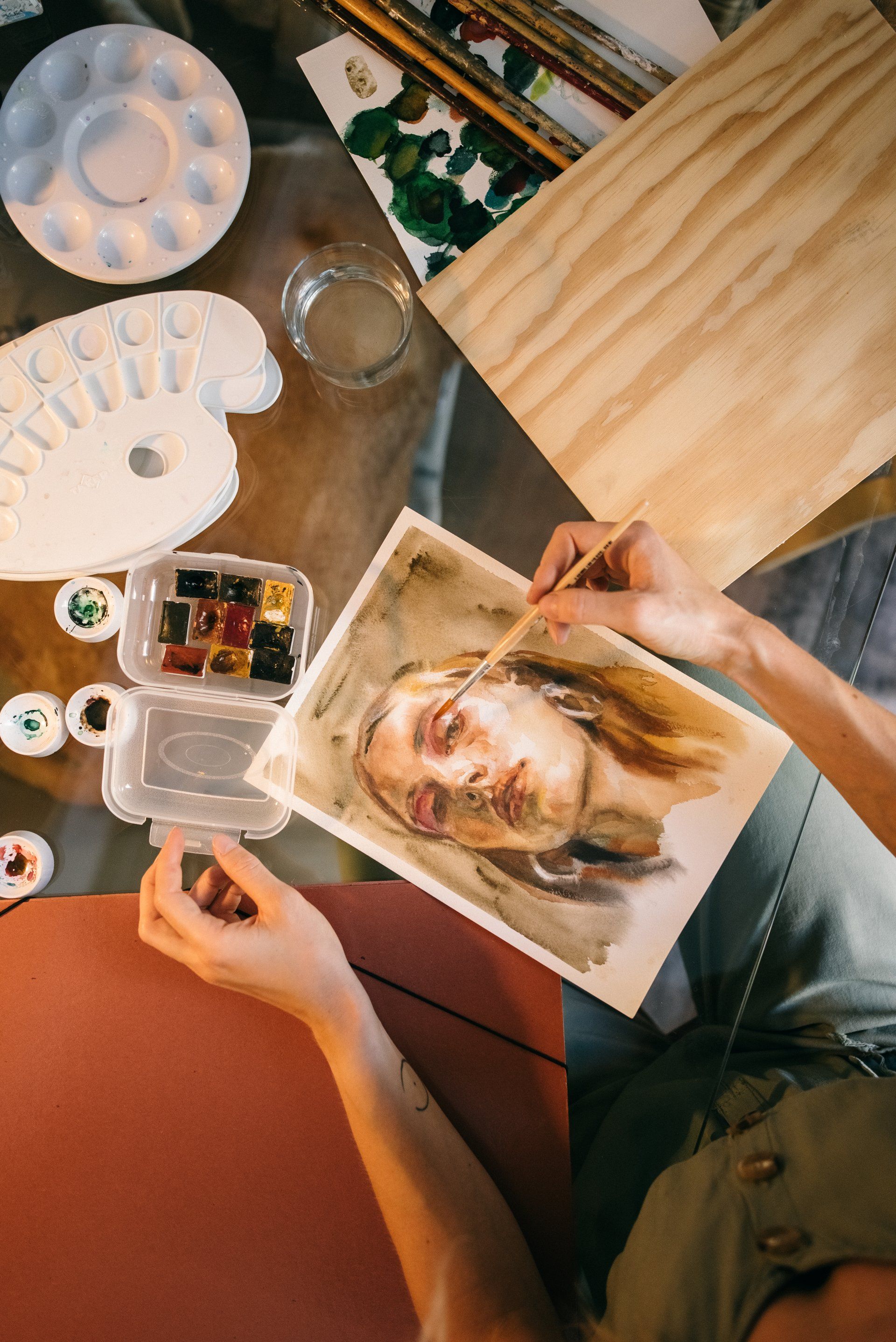 Une femme est assise à une table en train de peindre un portrait de femme.
