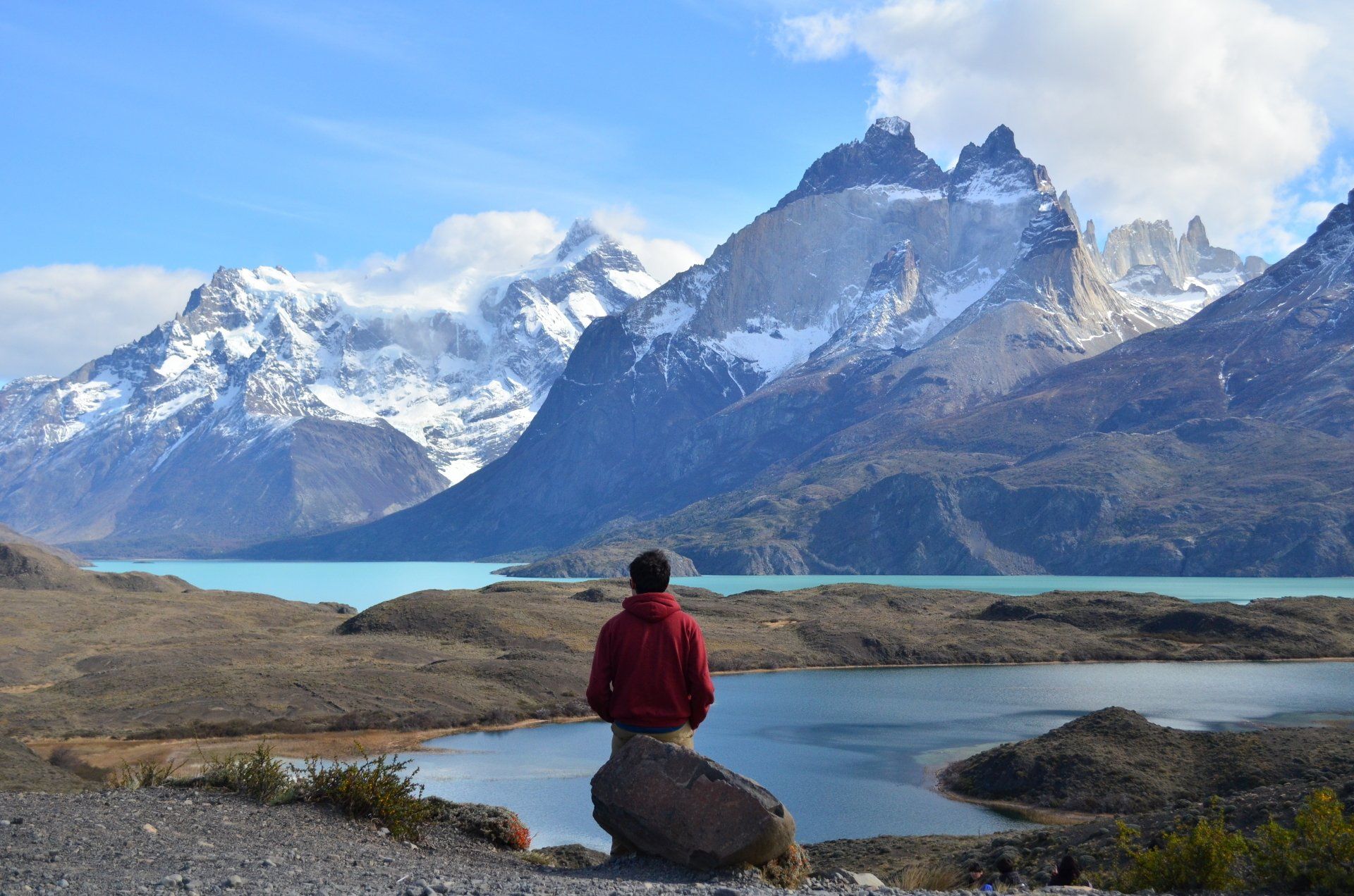 A man sitting by a lake viewing the Andes Mountains in the distance