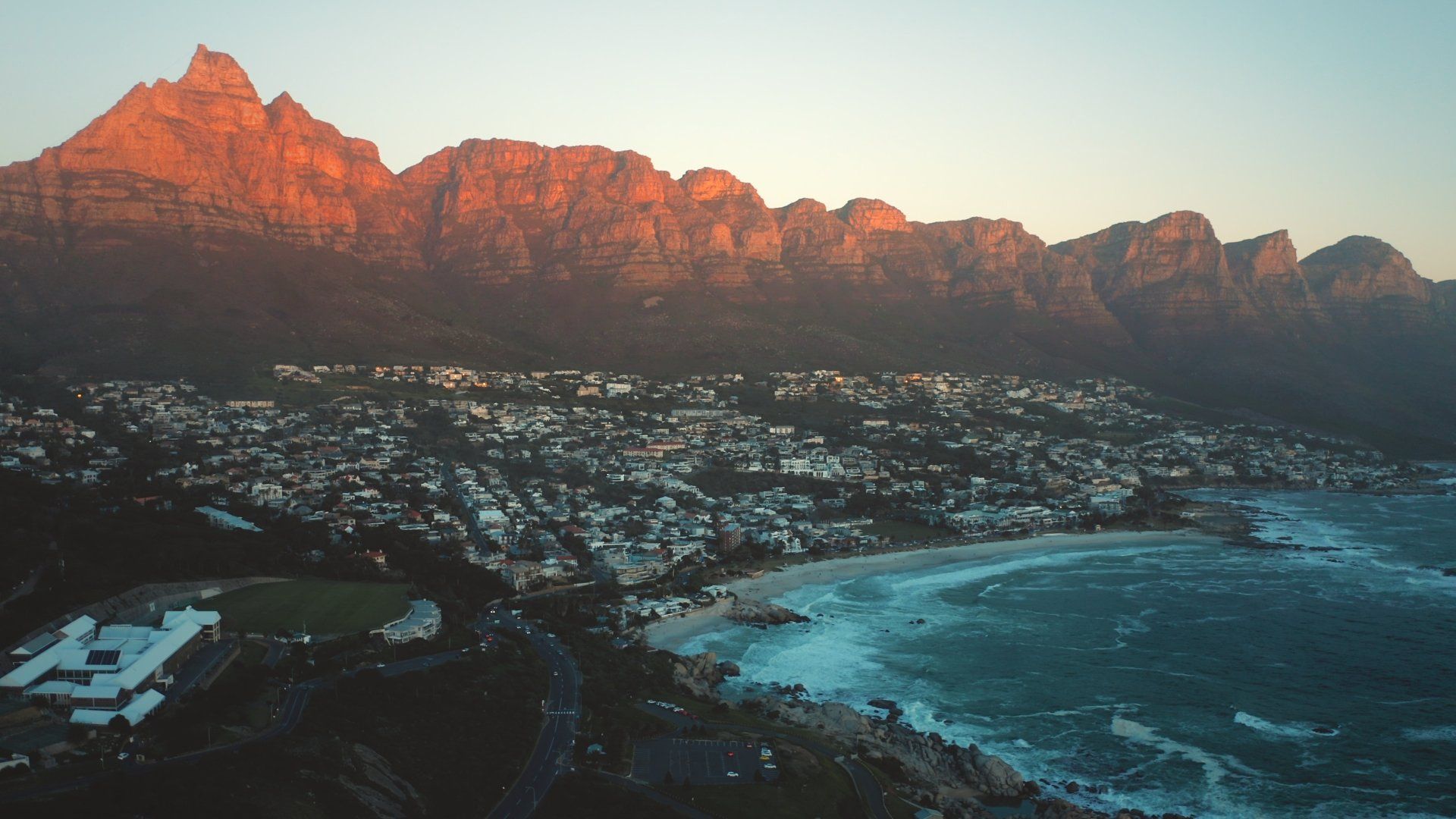 An aerial view of a city next to a body of water with mountains in the background.